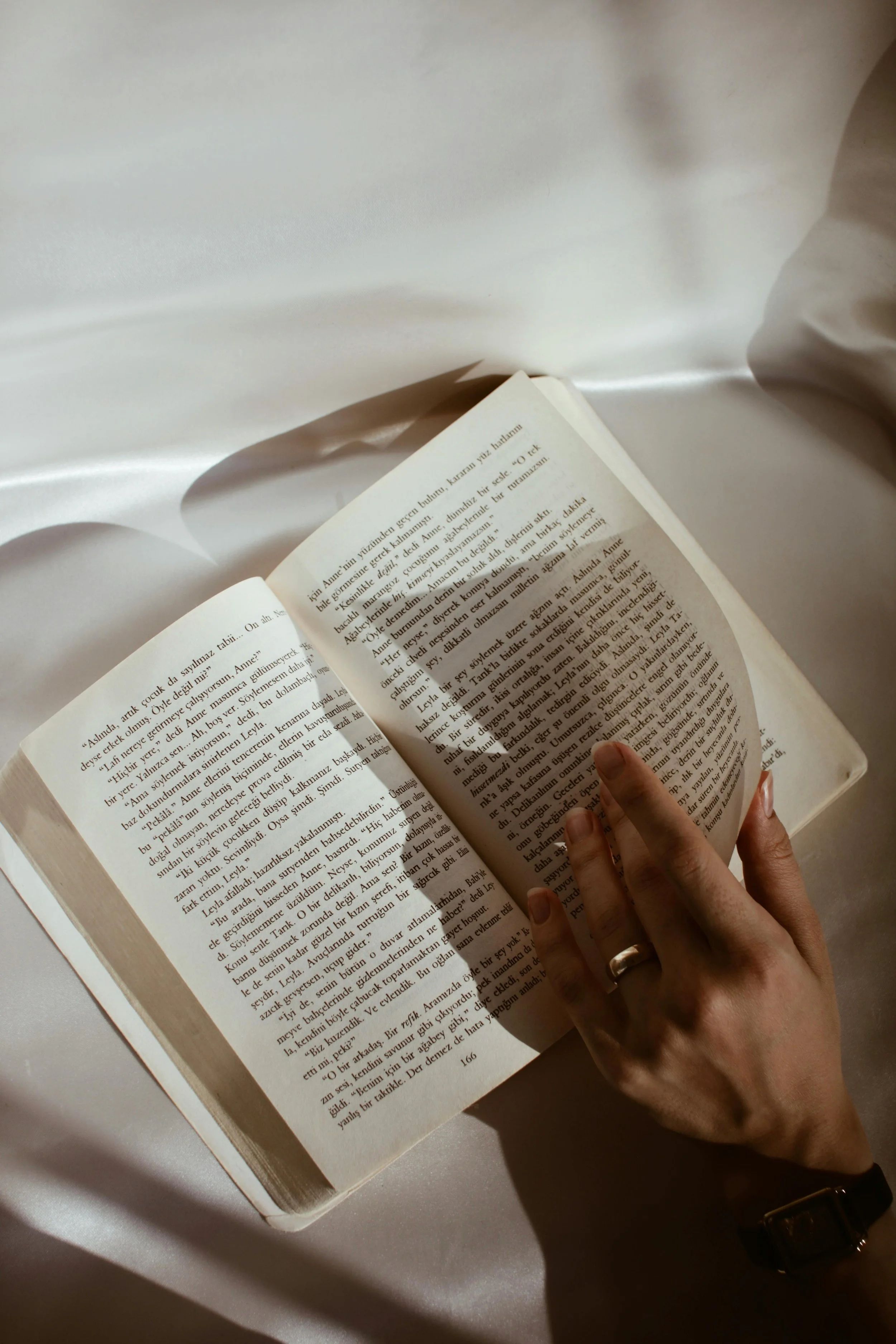 Une personne tient un livre ouvert avec une main, sur un fond blanc avec des ombres de lumière.