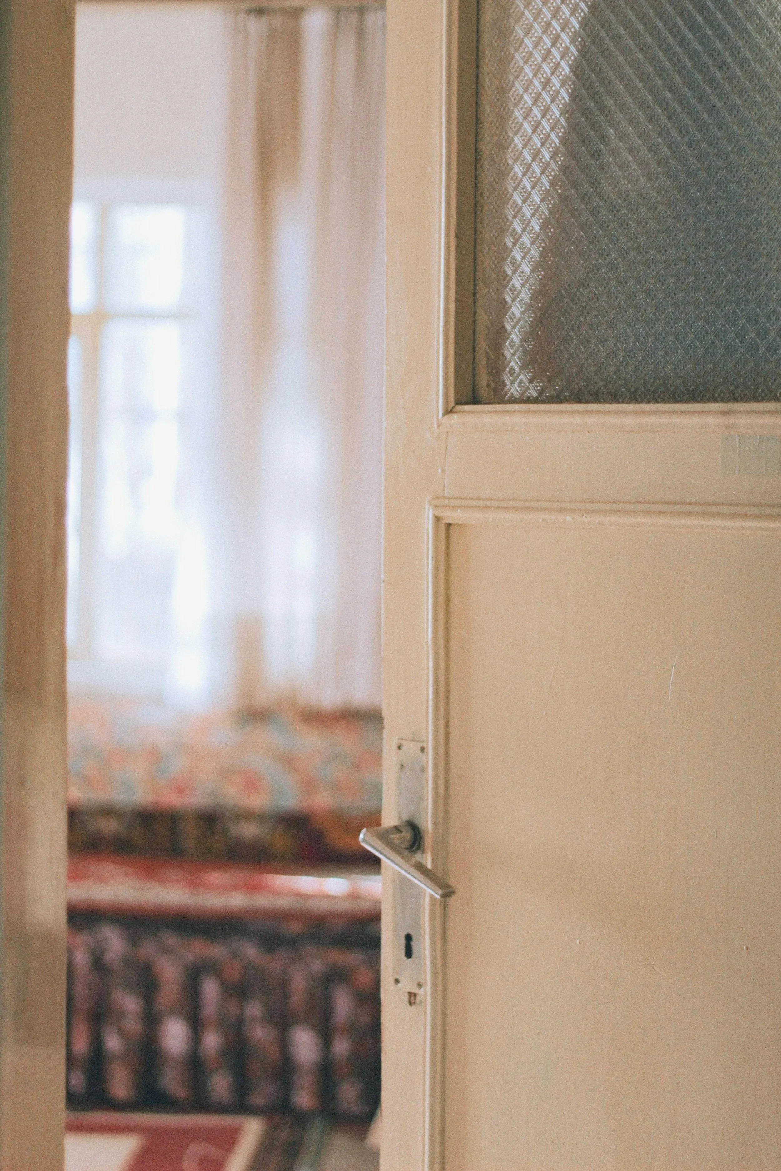 Une porte partiellement ouverte donnant sur une pièce avec un tapis aux motifs colorés et des rideaux légers en arrière-plan.