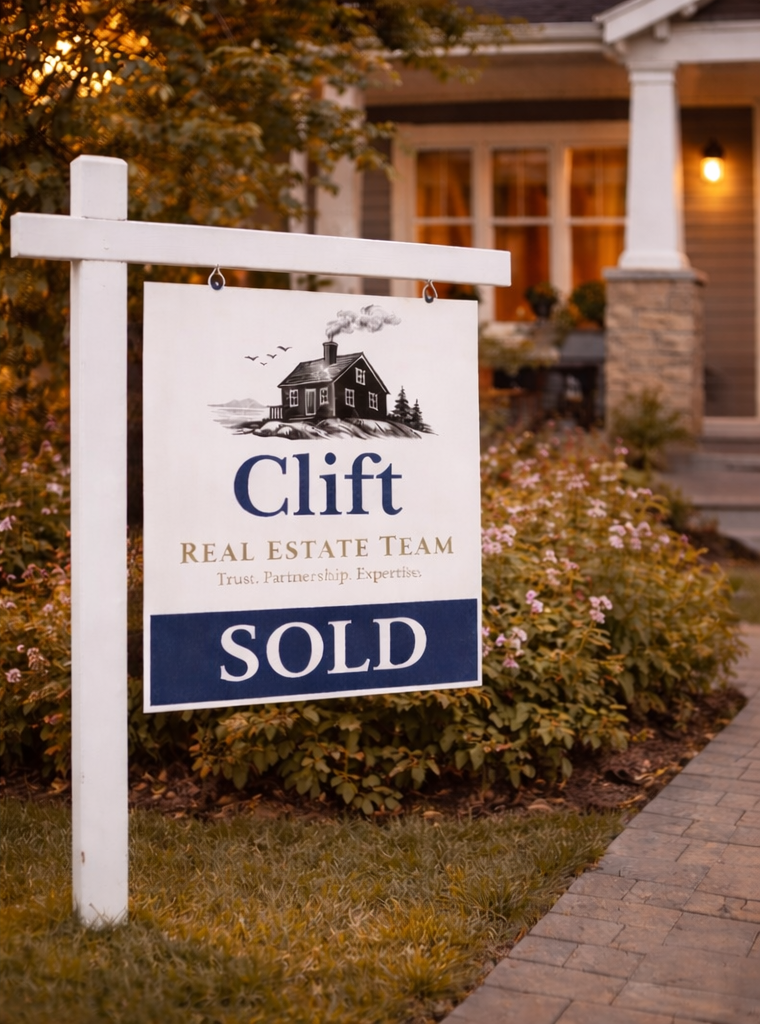 A yard sign indicating a house has been sold by Clift Real Estate Team, with a house and garden in the background at dusk.