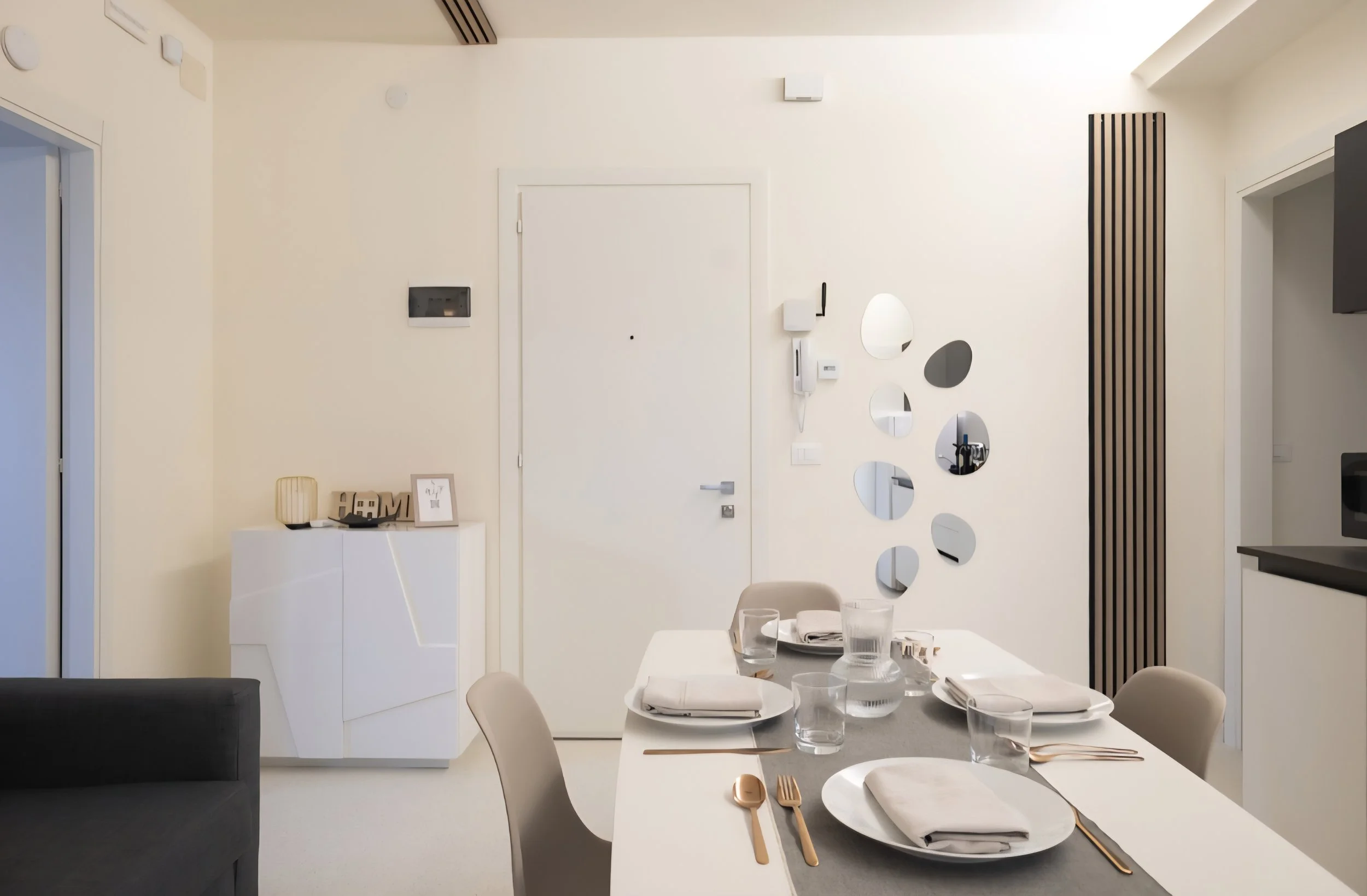 Sala da pranzo moderna con tavolo apparecchiato, sedie beige, specchi decorativi sulla parete e pannelli di legno verticale.