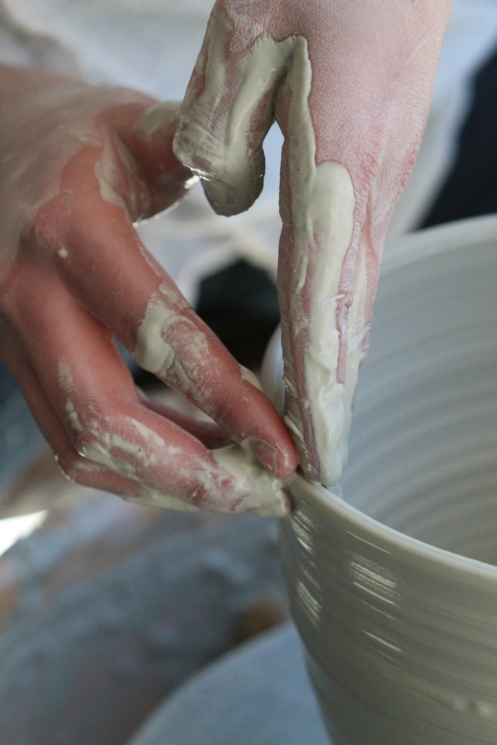 Close-up of hands shaping a ceramic vase on a pottery wheel with wet clay.