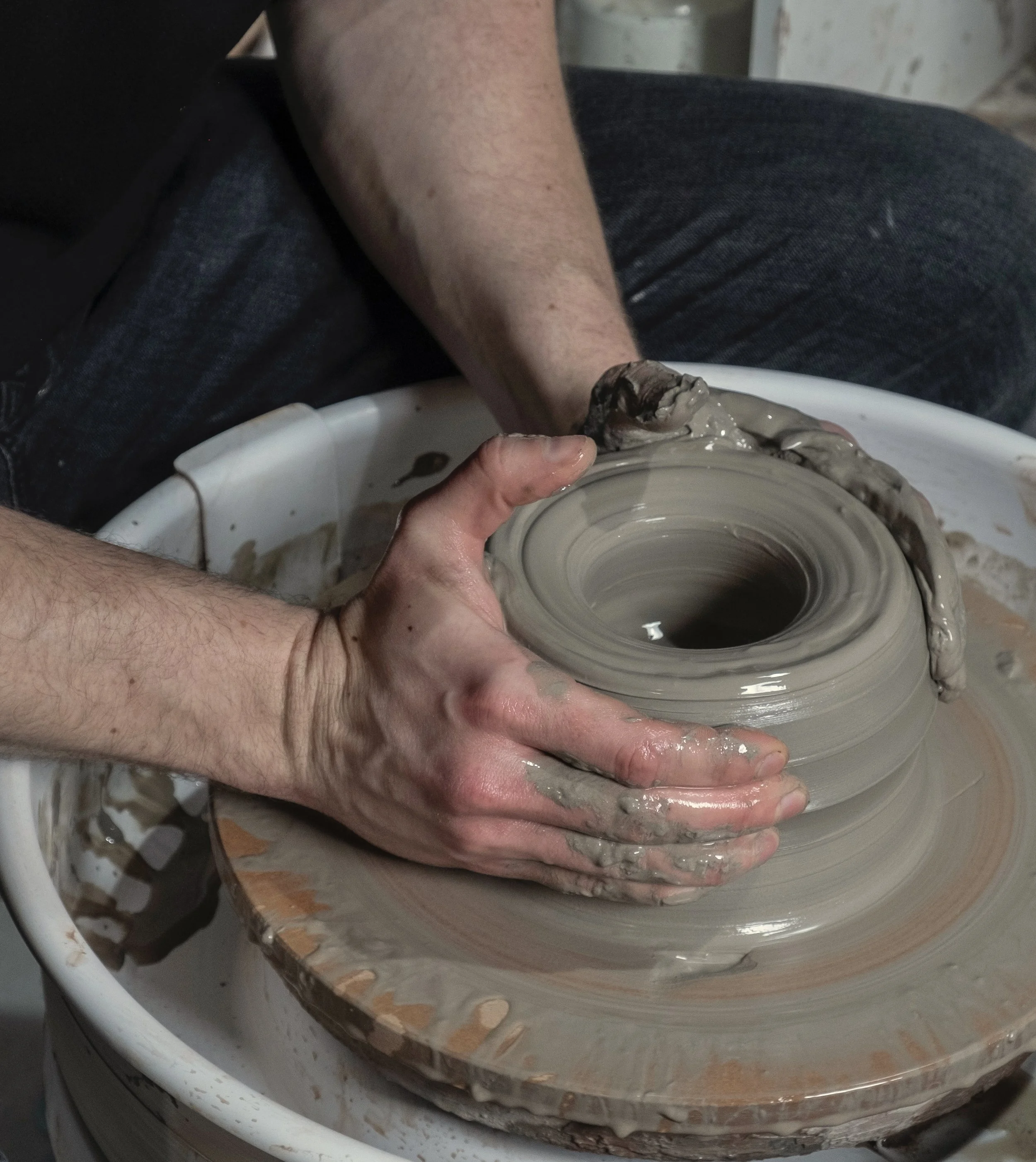 A person wheel-throwing pottery with clay on their hands