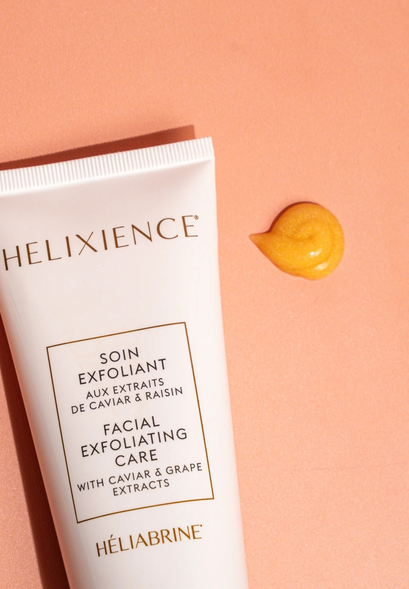 Tube de soin exfoliant avec extrait de caviar et raisin, placé à côté d'une goutte d'extrait de même composition, sur une surface rose pâle