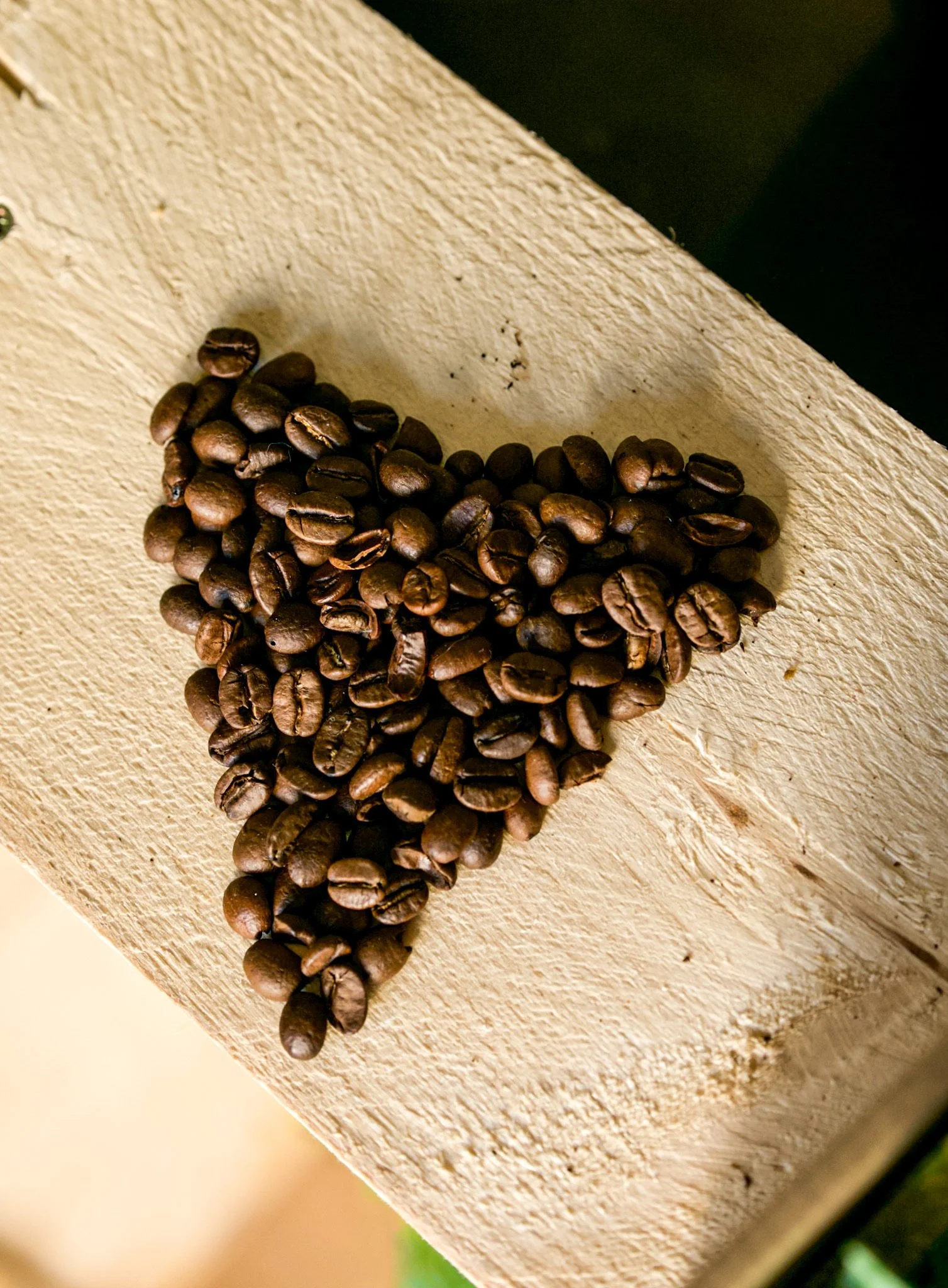 Grains de café disposés en forme de cœur sur une surface en bois.
