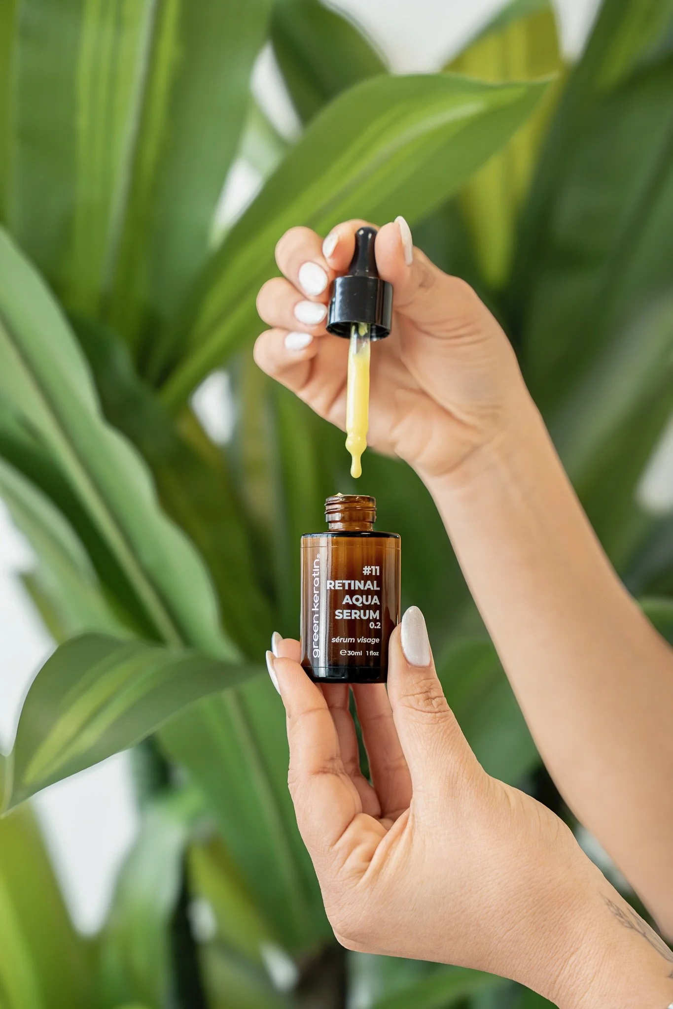 Une main tenant un flacon de sérum pour le visage avec une pipette, en arrière-plan des feuilles vertes d'une plante