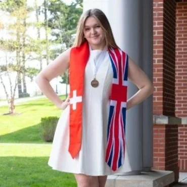 Young woman standing outdoors, wearing a white dress, with an England scarf and a medal around her neck.