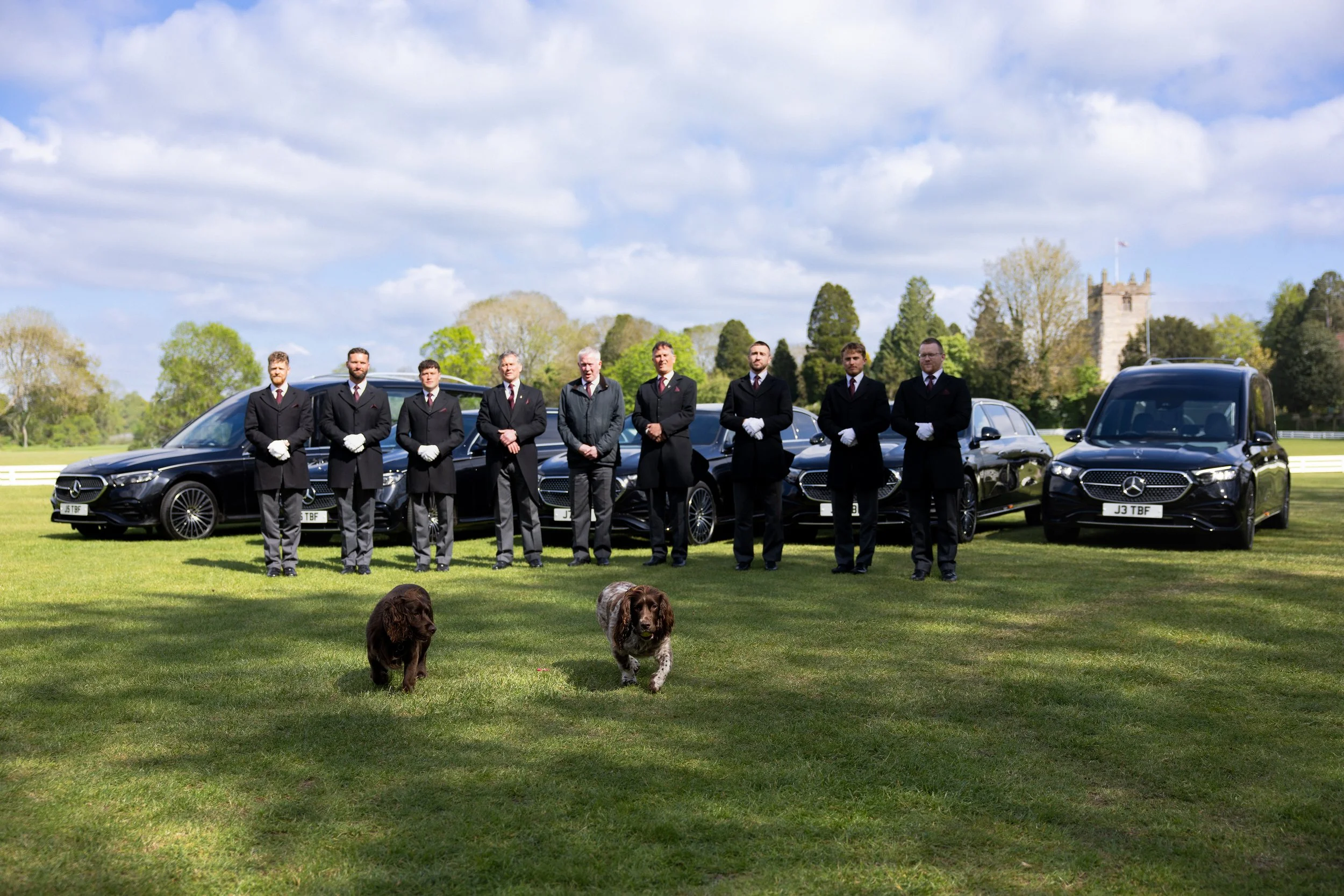 Thomas Brothers Funeral Directors in black suits and white gloves standing in front of luxury black hearses and limousines.