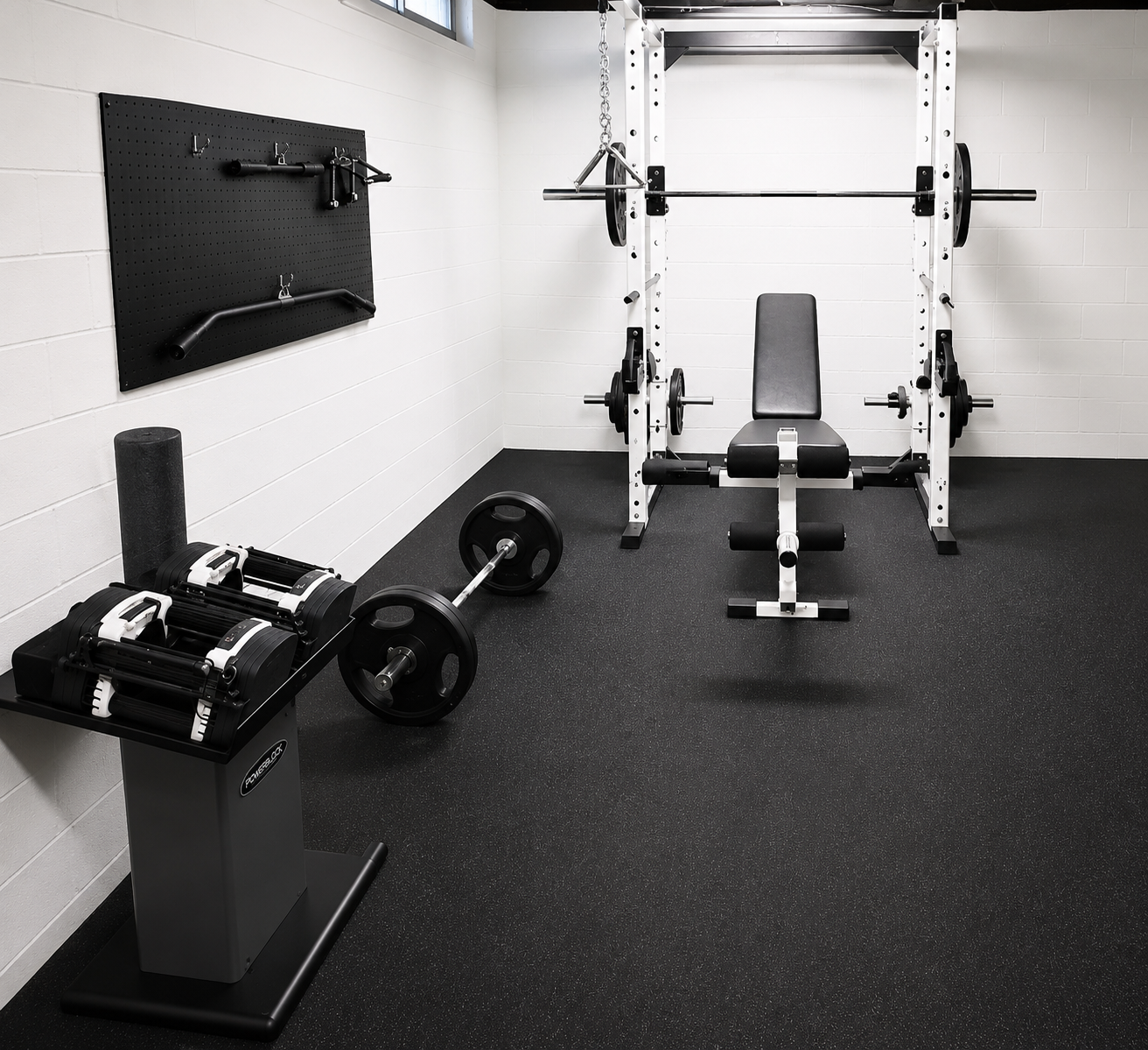 Empty workout room with a weight bench, barbell weights, weight plates, a foam roller, and hand grips, with a pegboard on the wall.