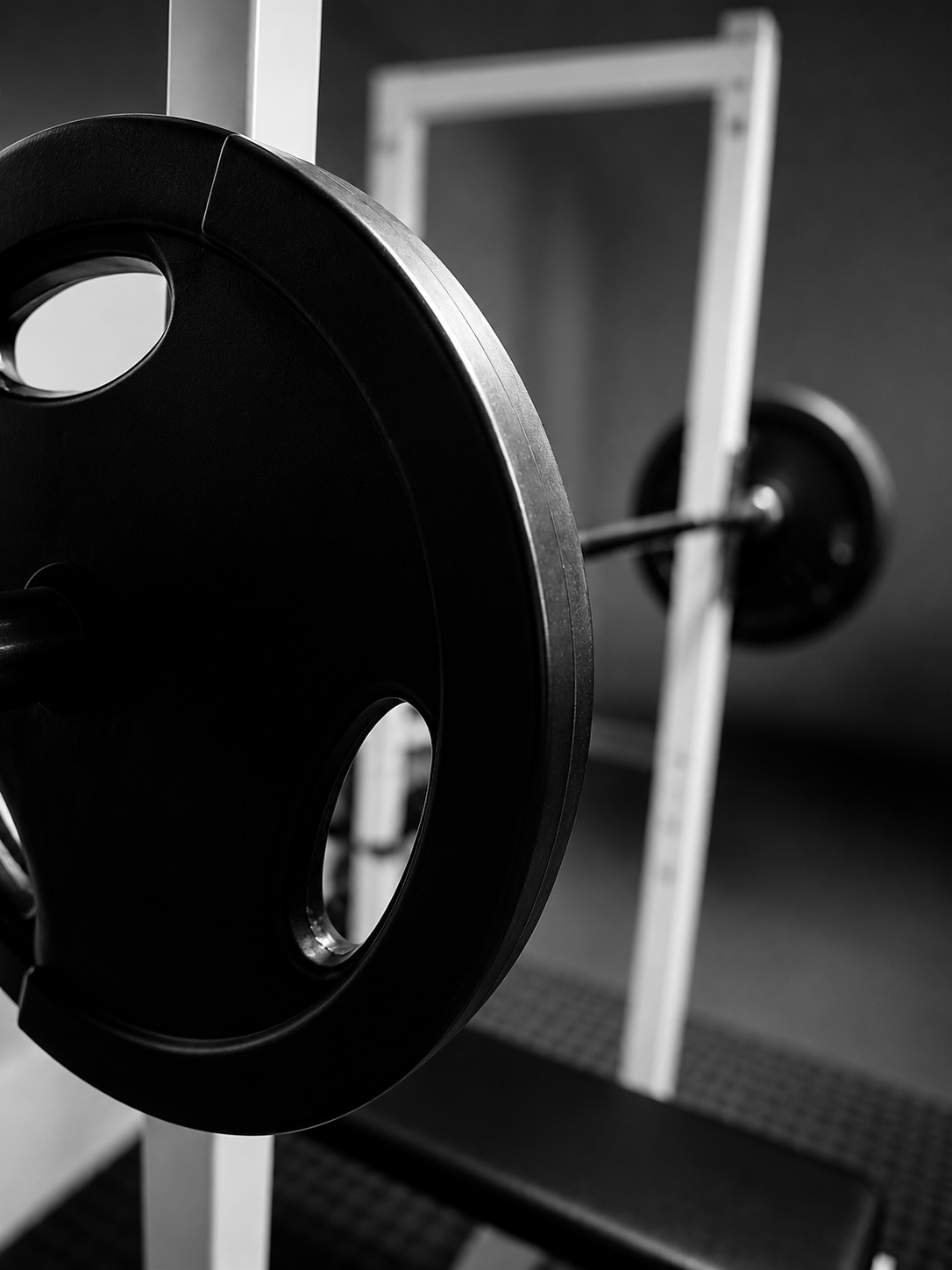 Close-up of a barbell with a weight plate in a gym setting, with another barbell visible in the background.