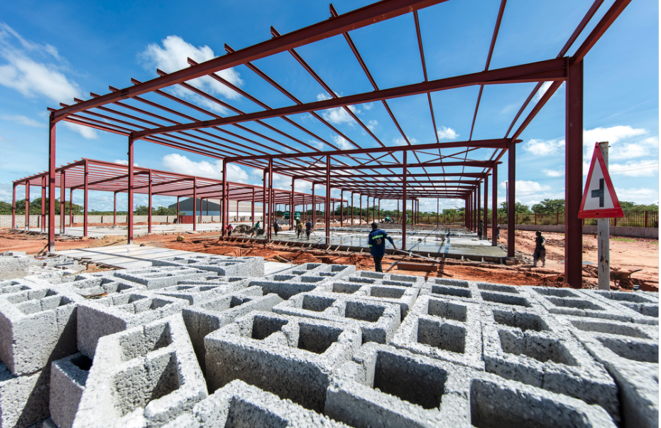 Roma Park Commercial Construction site with a steel framework for a building under construction, cinder blocks in the foreground, and construction workers working on the site under a partly cloudy sky.