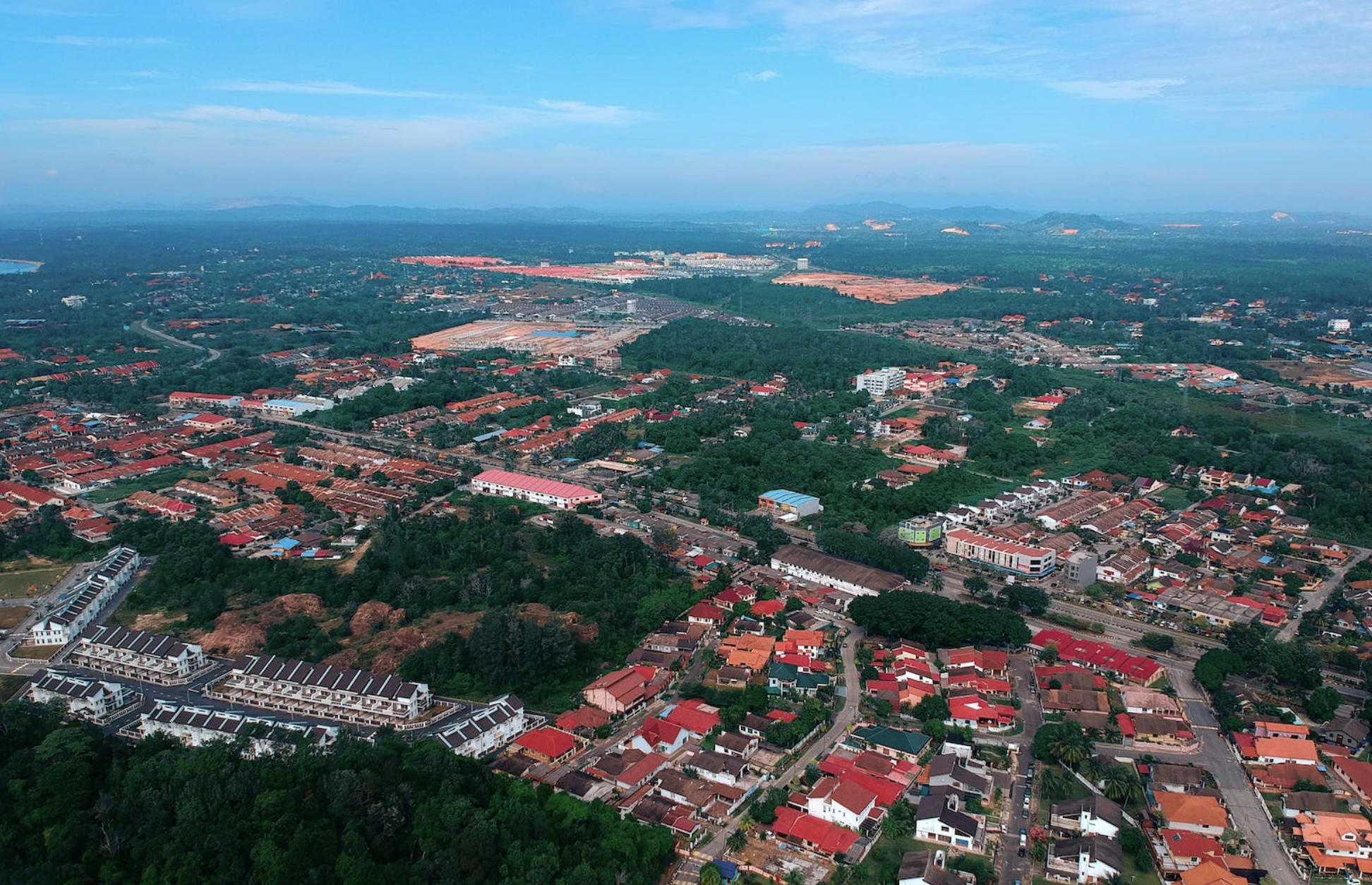 Aerial view of Kitwe with red-roofed houses, green trees, and roads, with a distant horizon under a partly cloudy sky.