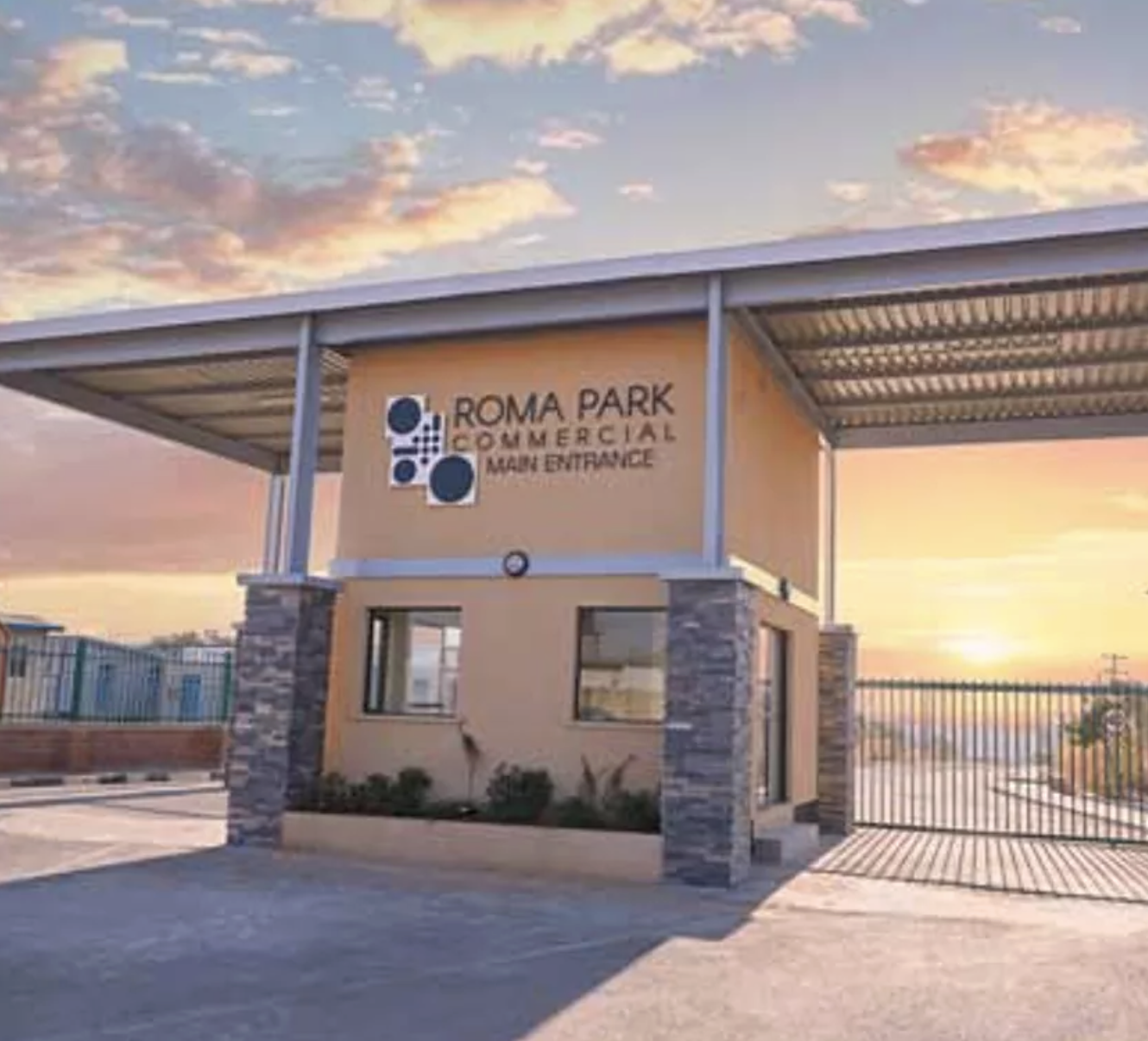 Entrance sign for Roma Park Commercial, showing a beige building with stone accents and a metal roof, against a sunset sky.