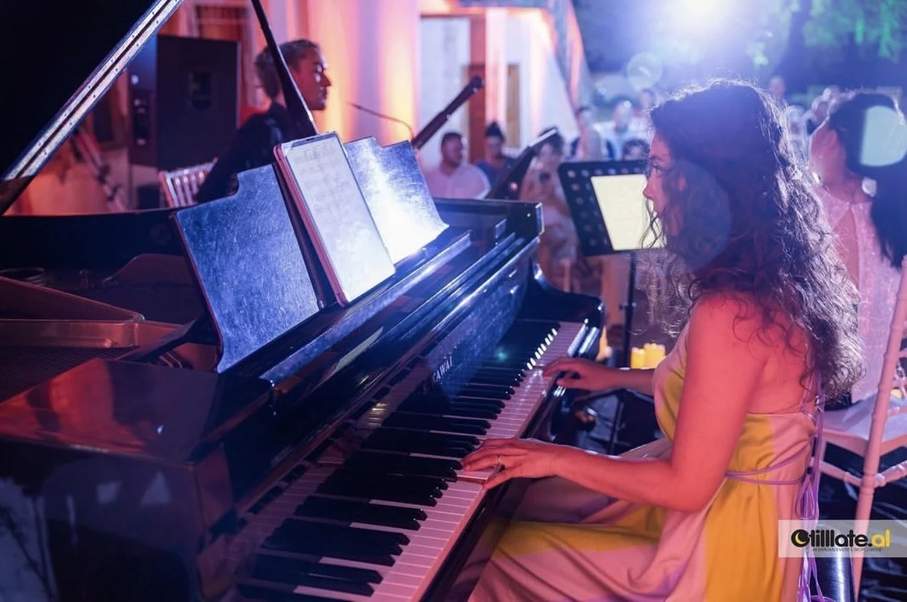 A woman in a yellow dress playing a black Yamaha grand piano at an outdoor event with people in the background.