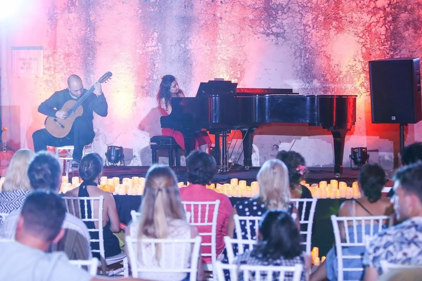Musicians performing on stage with candles and audience watching.