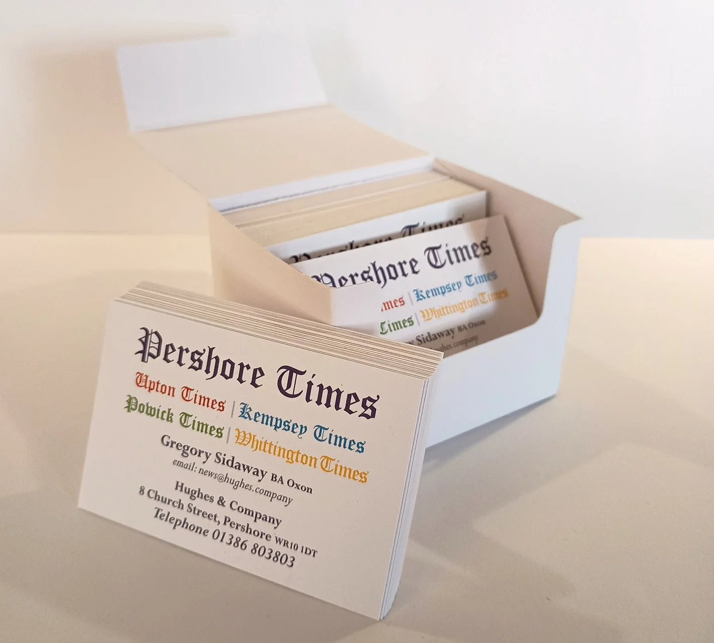 Business card for Pershore Times with contact details, placed in front of a white box containing multiple copies of the same card.