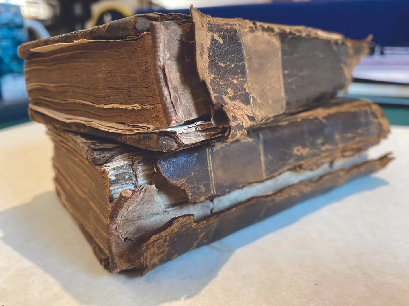 An old, worn-out, stack of three antique books with tattered, discolored leather covers, placed on a flat surface.
