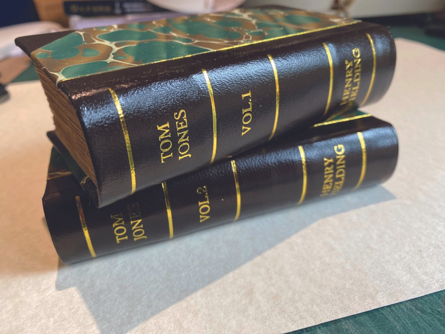 Two hardcover books stacked on top of each other with black covers and gold lettering, titled "TOM JONES VOL. 1" and "TOM JONES VOL. 2". The top book has a decorative green and gold marbled endpaper visible at the top.