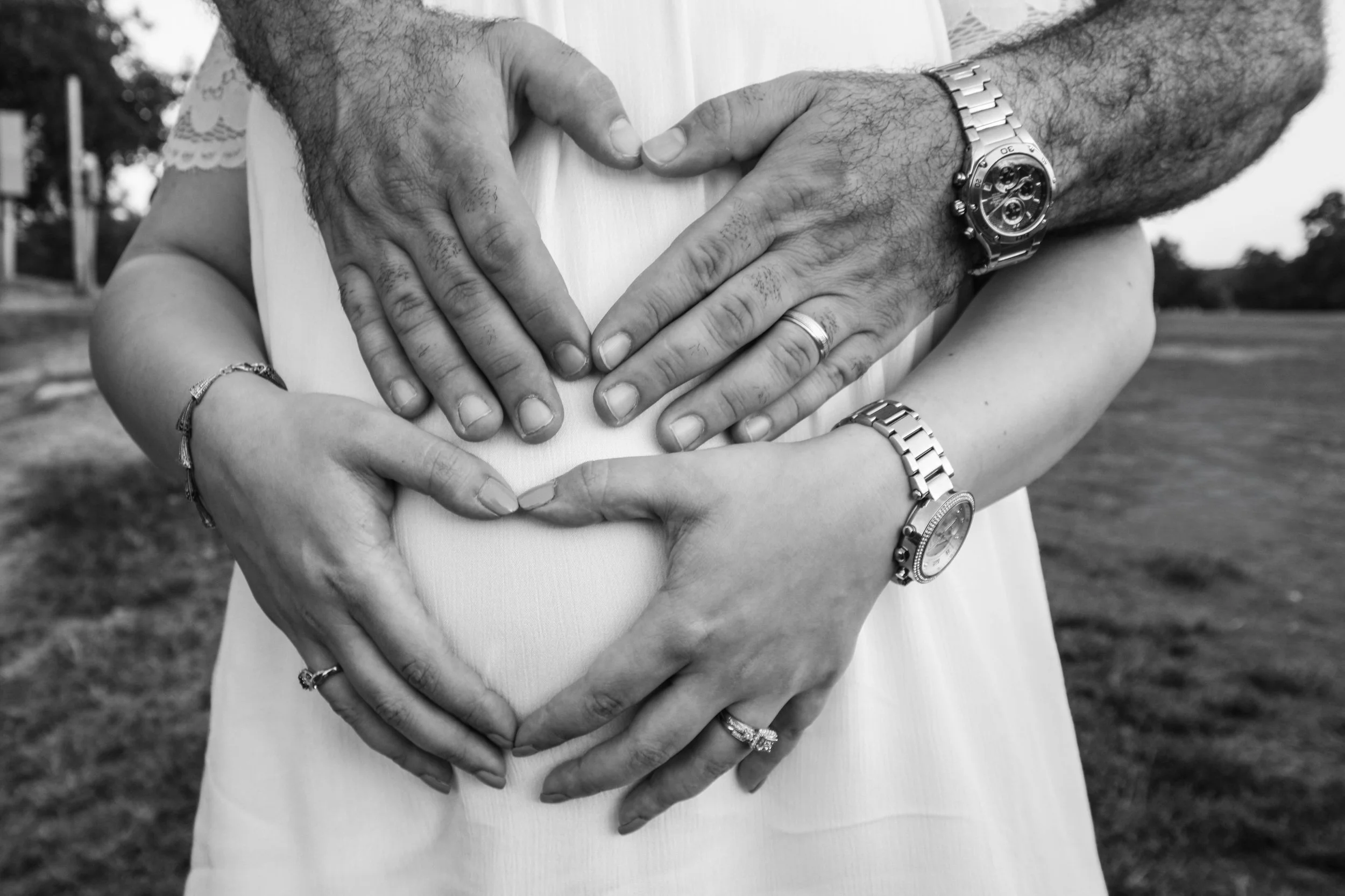 Black and white maternity close-up showing expecting parents forming a heart shape around a baby bump during a maternity photography session in Austin, Texas. Emotional pregnancy photography captured by Caerus Multimedia.