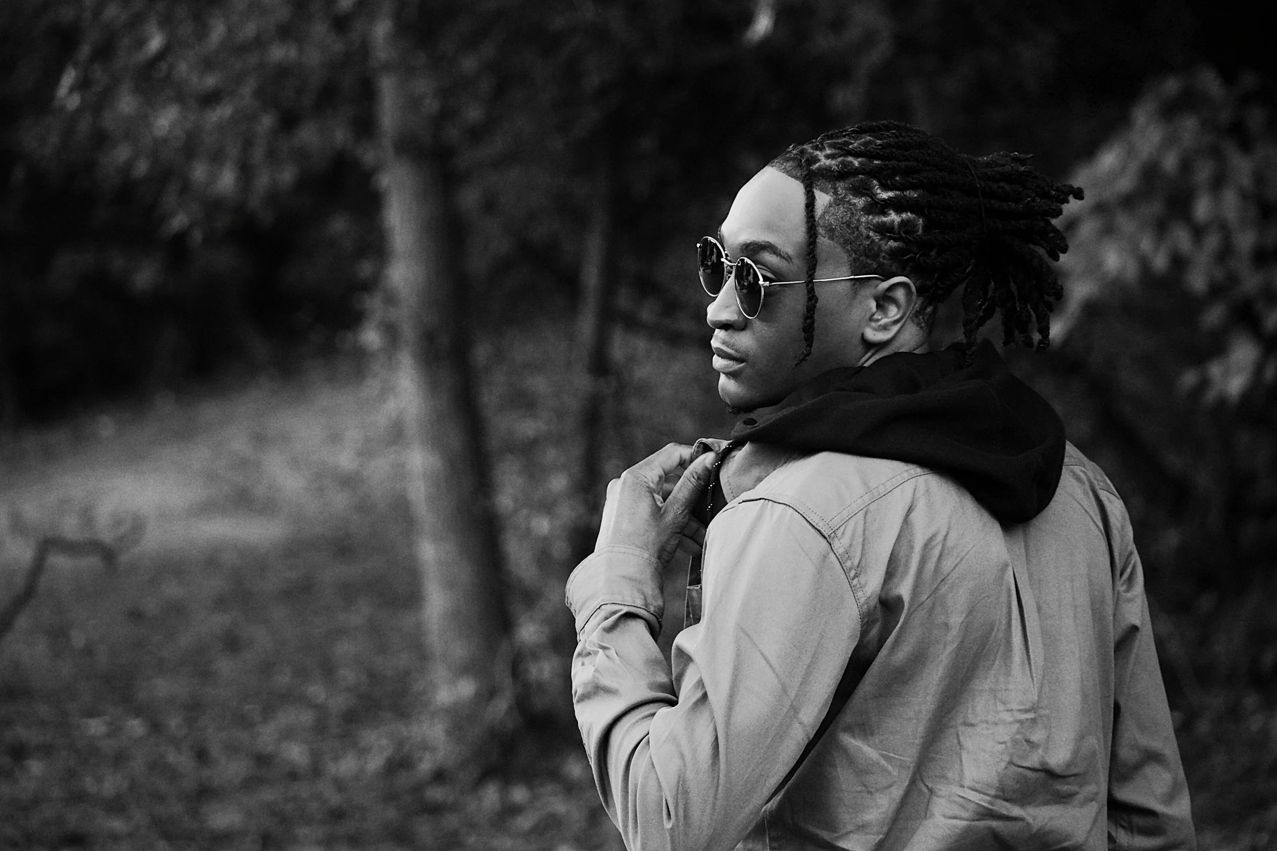 A cinematic black and white portrait captured in a wooded setting. The subject’s pose and lighting create a dramatic mood that emphasizes personality, texture, and timeless portrait storytelling.