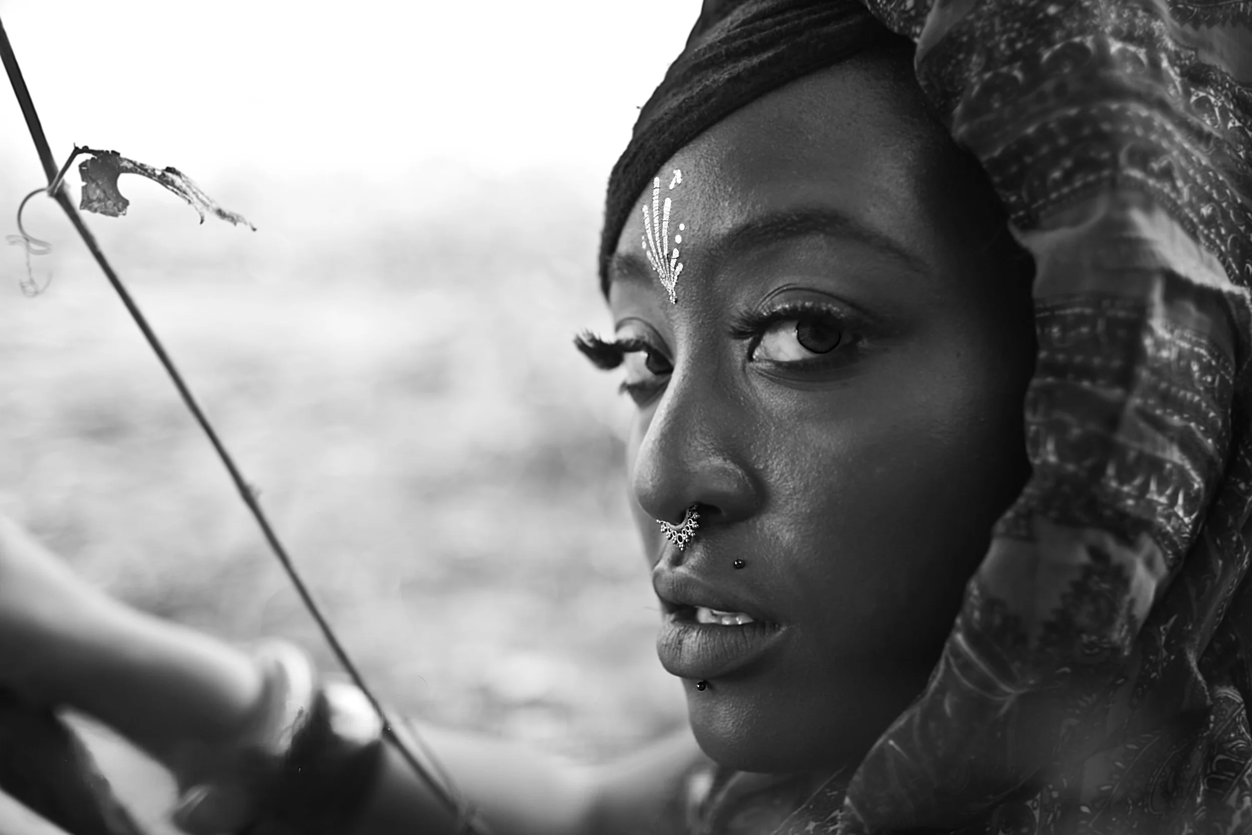 In this intimate black-and-white portrait, the Queen’s expression reveals quiet strength and contemplation. The golden symbol becomes a focal point, representing wisdom, resilience, and the inner light carried throughout the series.