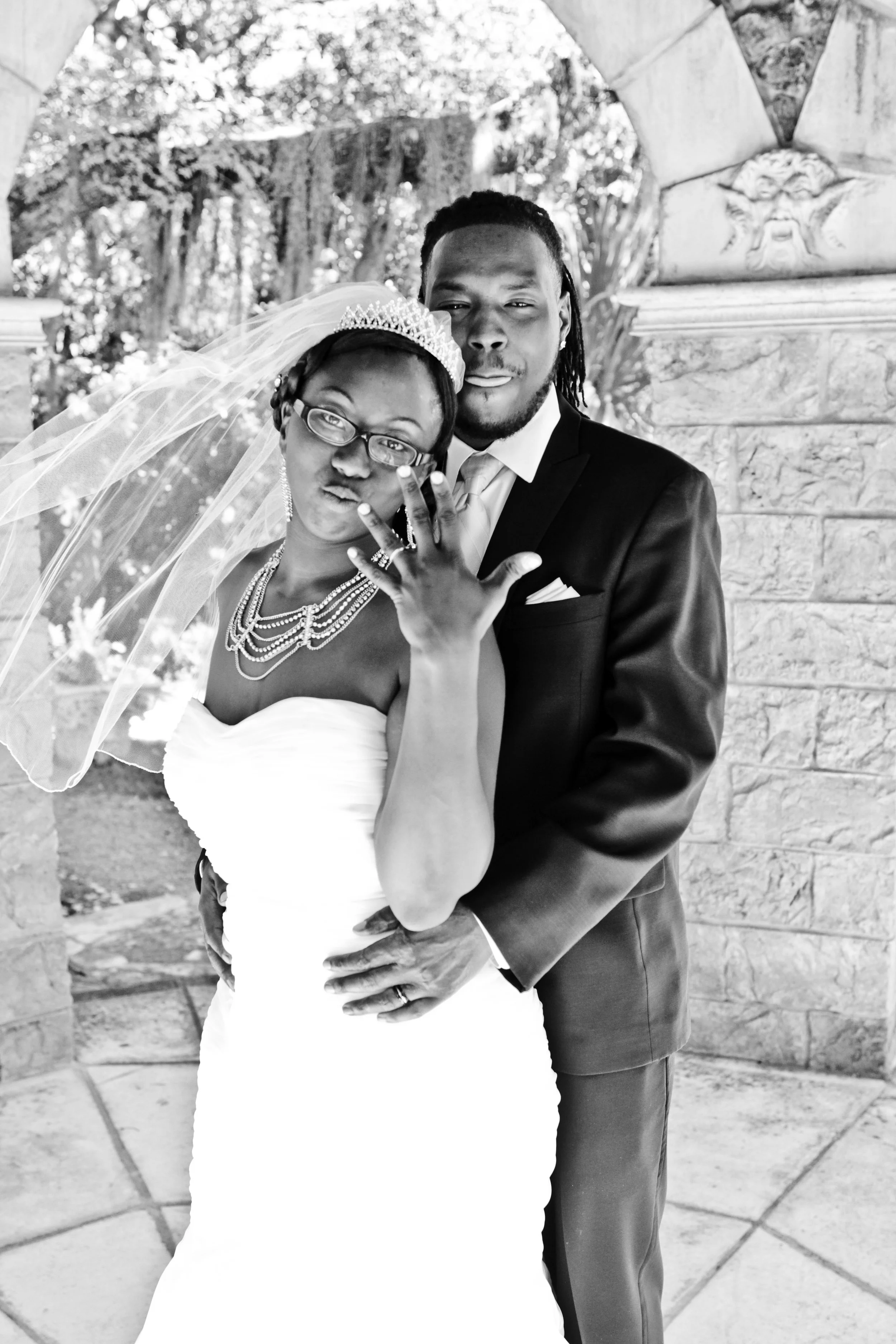 The bride proudly displays her wedding ring while standing beside her groom beneath a garden archway. Captured by Caerus Multimedia, this portrait highlights the excitement and symbolism of the wedding day.