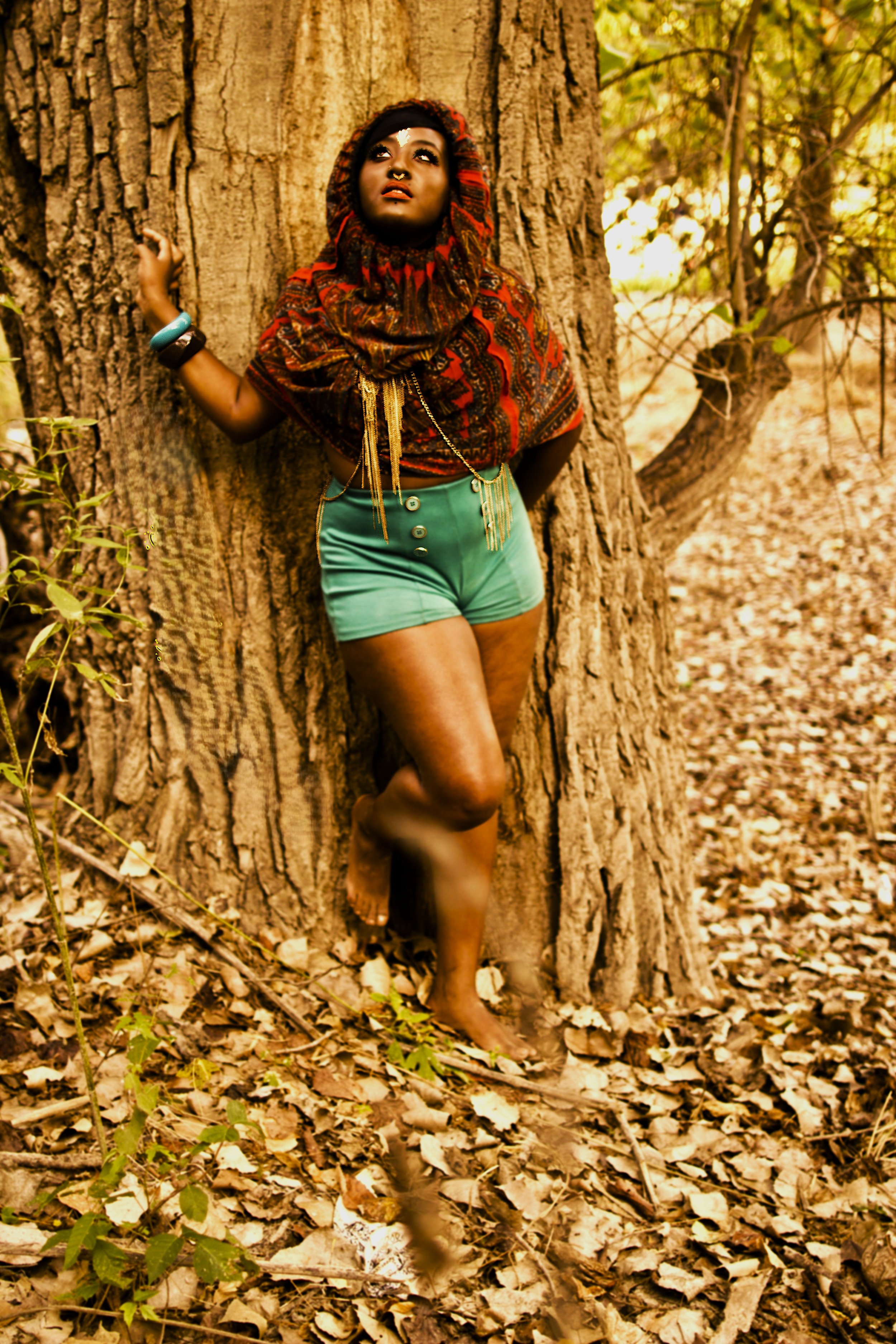 Standing against the strength of an ancient tree, the Queen of the Golden Sun looks upward as light filters through the forest canopy. The earthy textures of the environment and the vibrant patterns of her garments create a powerful contrast, symboli