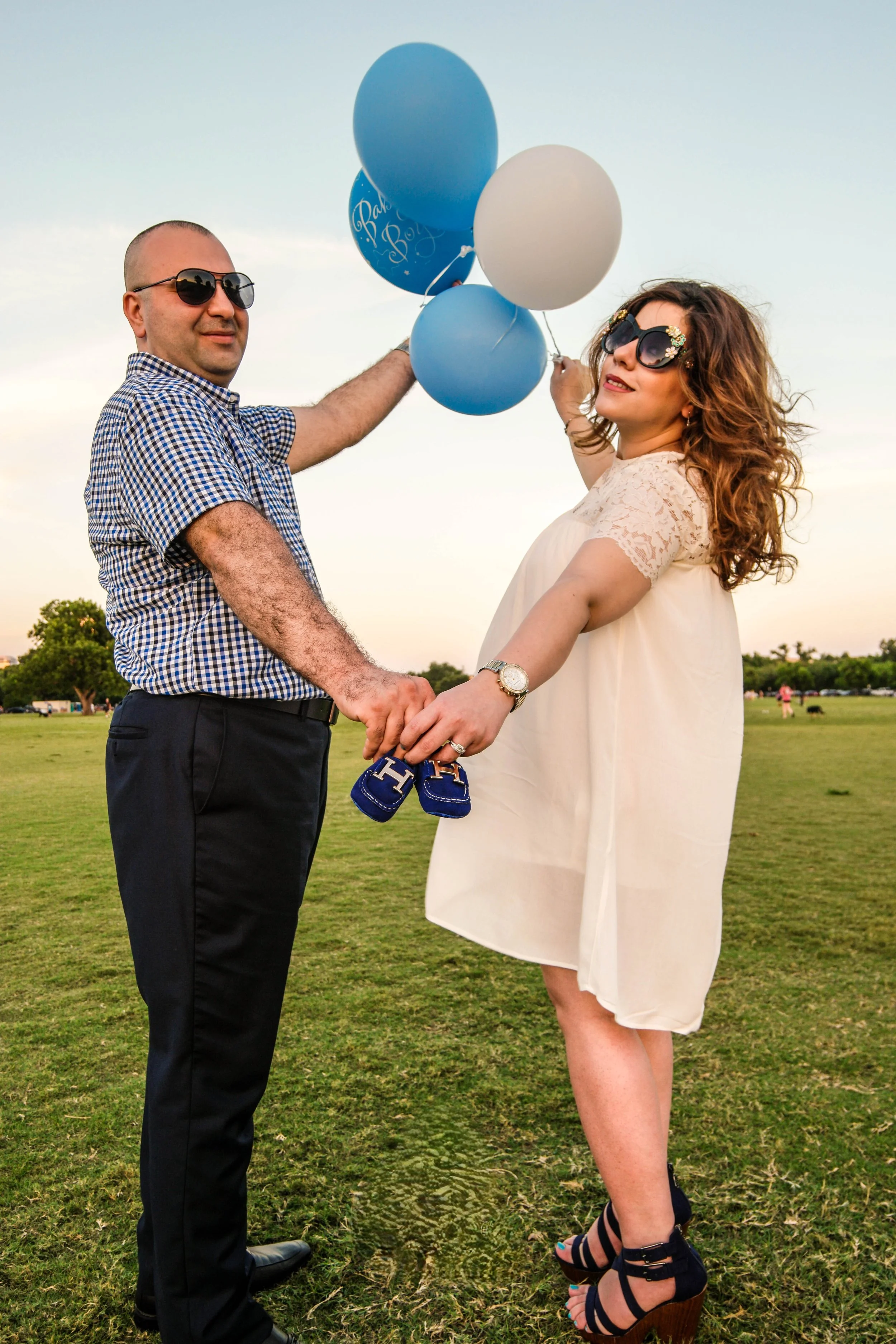 Joyful maternity announcement photo of expecting parents holding baby shoes and balloons during a maternity photography session in Austin, Texas captured by Caerus Multimedia, an Austin maternity photographer.