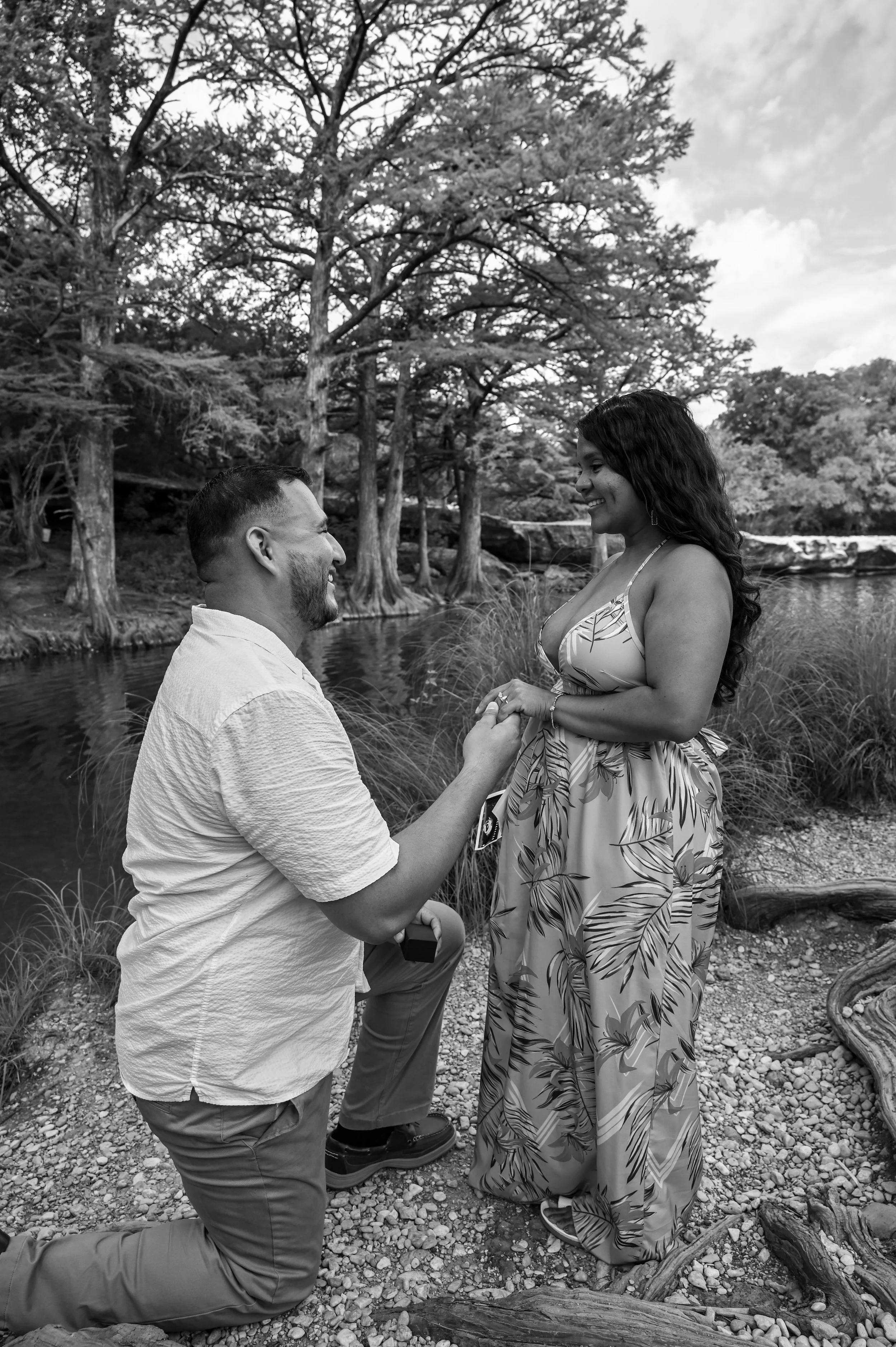 A joyful engagement photography moment captured as the groom places the engagement ring on his partner's hand during a romantic proposal beside a peaceful Austin creek, photographed by Caerus Multimedia.