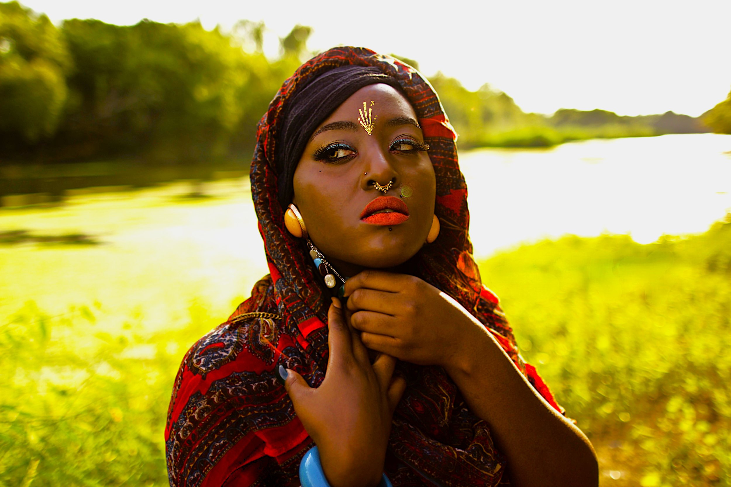 In this moment from the Queen of the Golden Sun series, the subject stands beside the water, illuminated by warm golden light. Her gaze carries both strength and mystery, symbolizing resilience and quiet authority within nature’s calm landscape.
