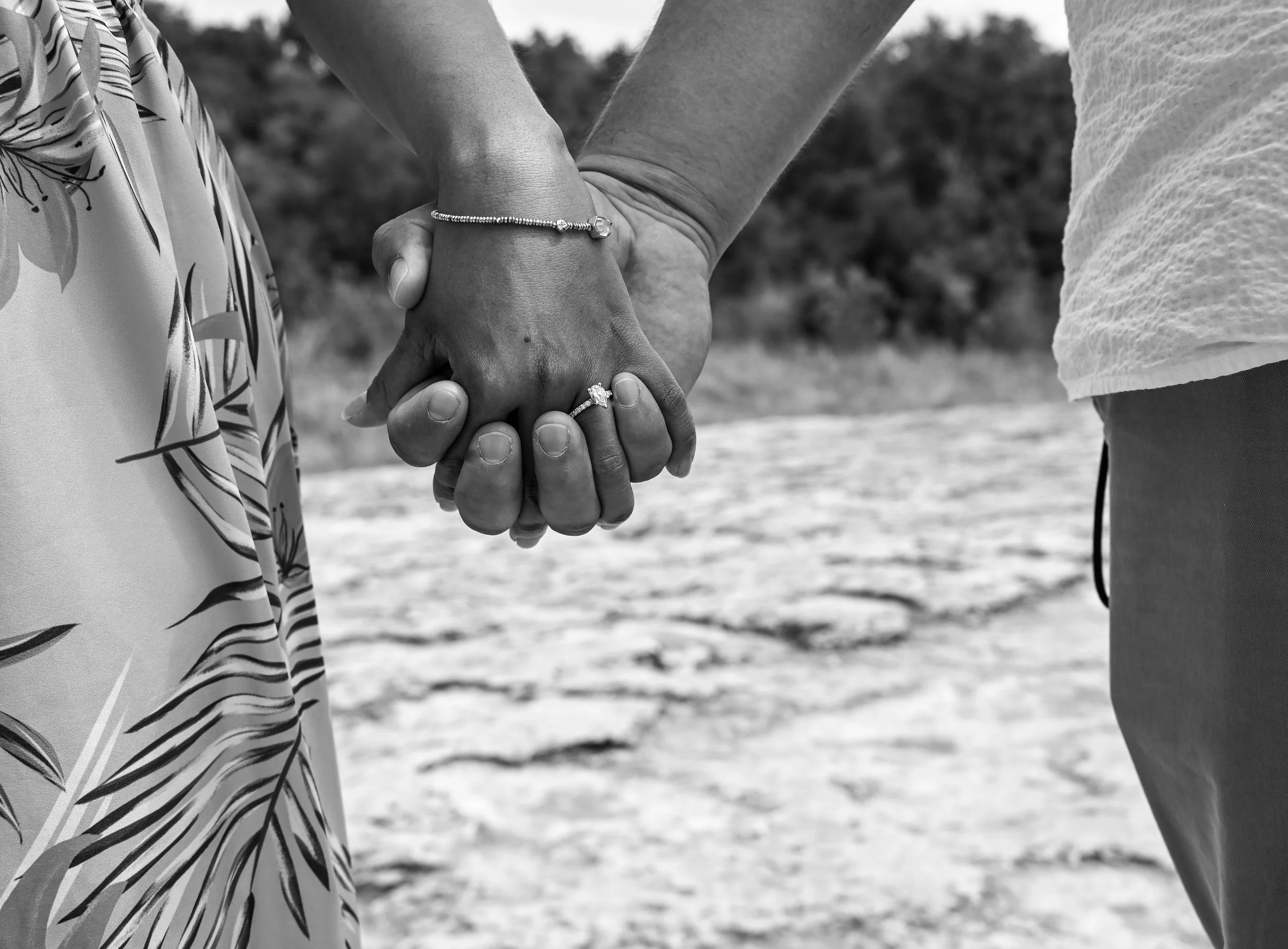 A close-up black and white engagement photo capturing a newly engaged couple holding hands and showcasing the engagement ring during a romantic outdoor proposal session photographed by Caerus Multimedia, an Austin engagement photographer specializing