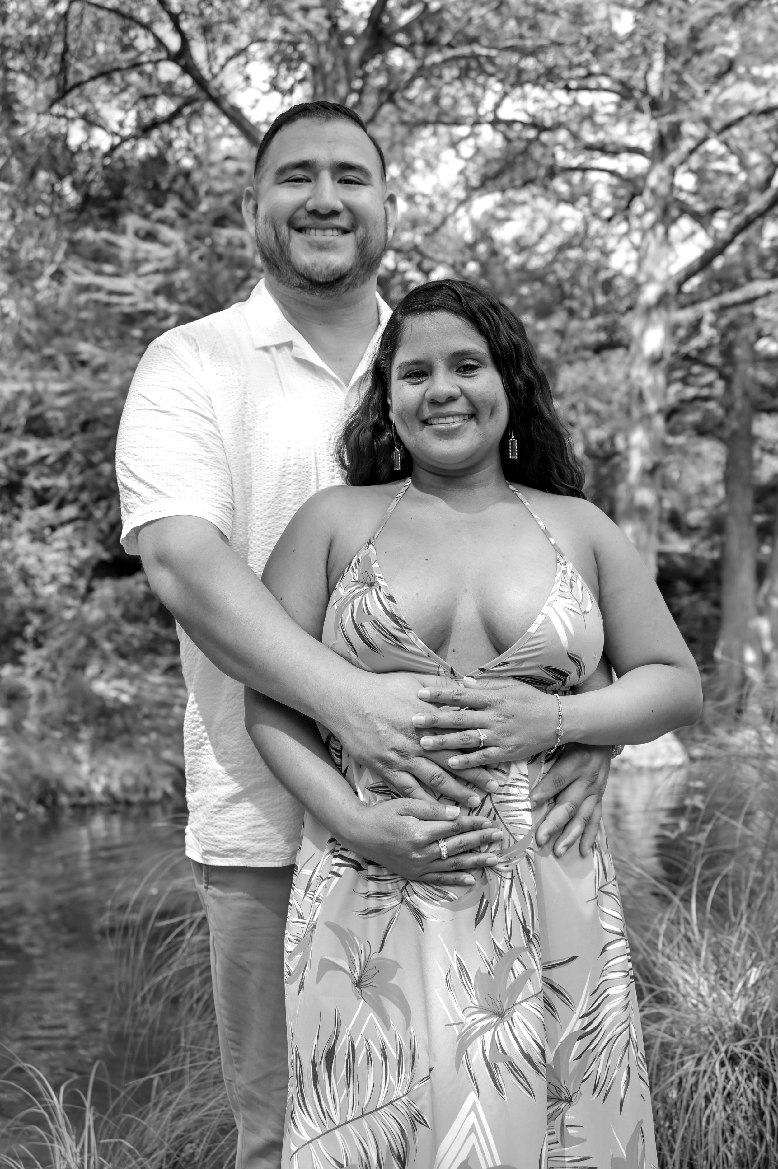 A romantic black and white engagement portrait of a couple embracing beside a peaceful creek in Austin, Texas. Captured by Caerus Multimedia, this natural engagement photography moment highlights genuine connection and timeless outdoor couples photog