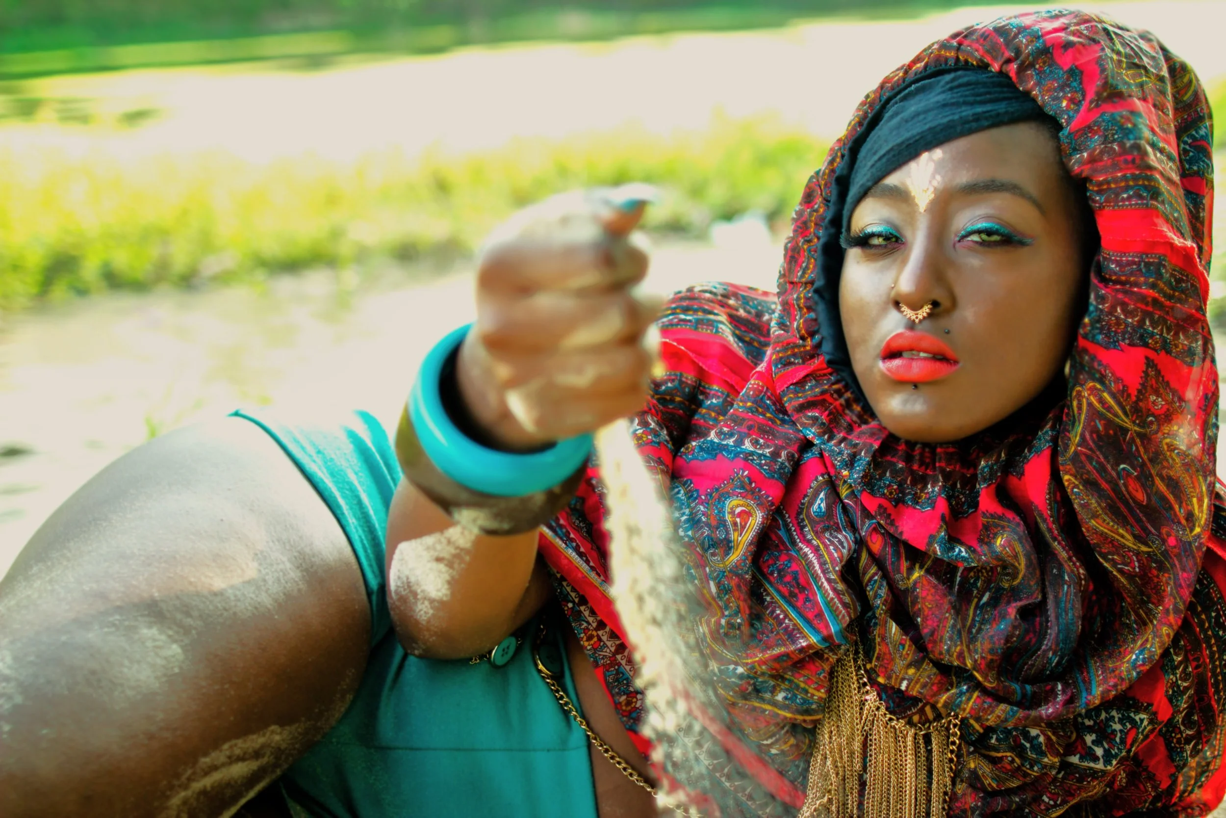 The Queen of the Golden Sun rests along the water’s edge, holding grains of sand as they slip through her fingers. In this quiet moment, time, nature, and identity intertwine, symbolizing the fleeting yet powerful nature of transformation.