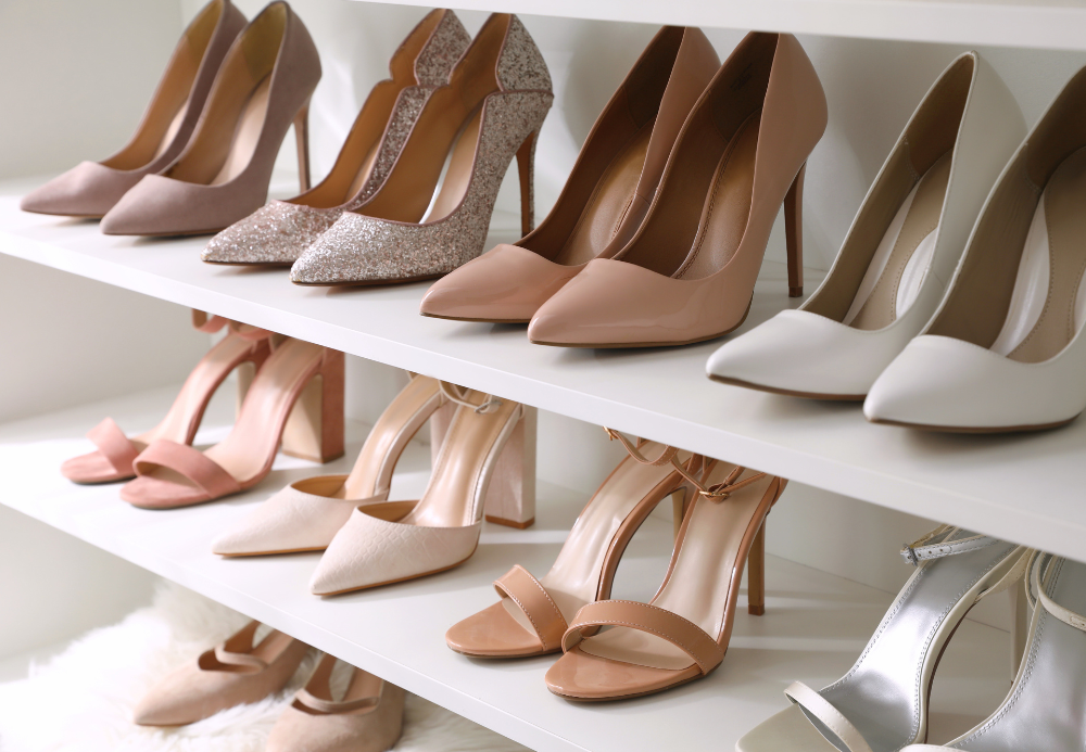 Three shelves of women's high-heeled shoes in neutral colors, including beige, pink, glittery, and white, displayed in a retail store.