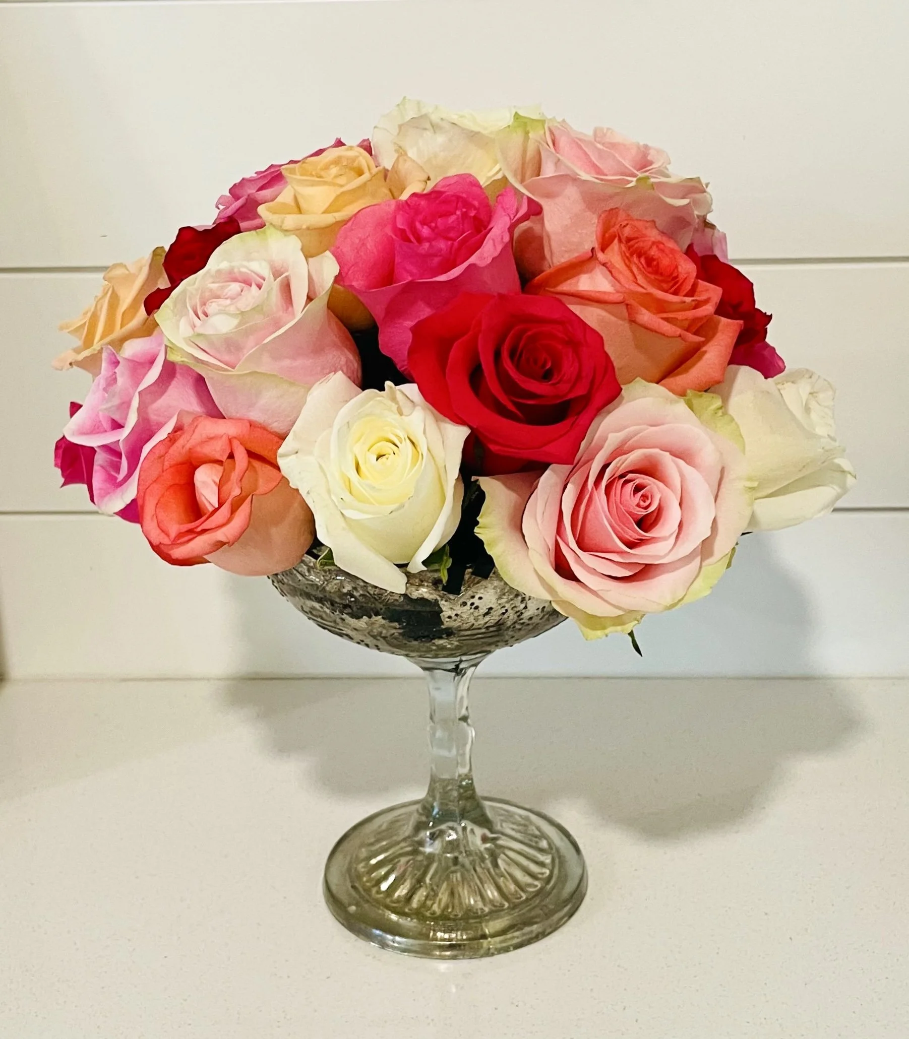 A bouquet of various colored roses in a glass bowl on a white surface.