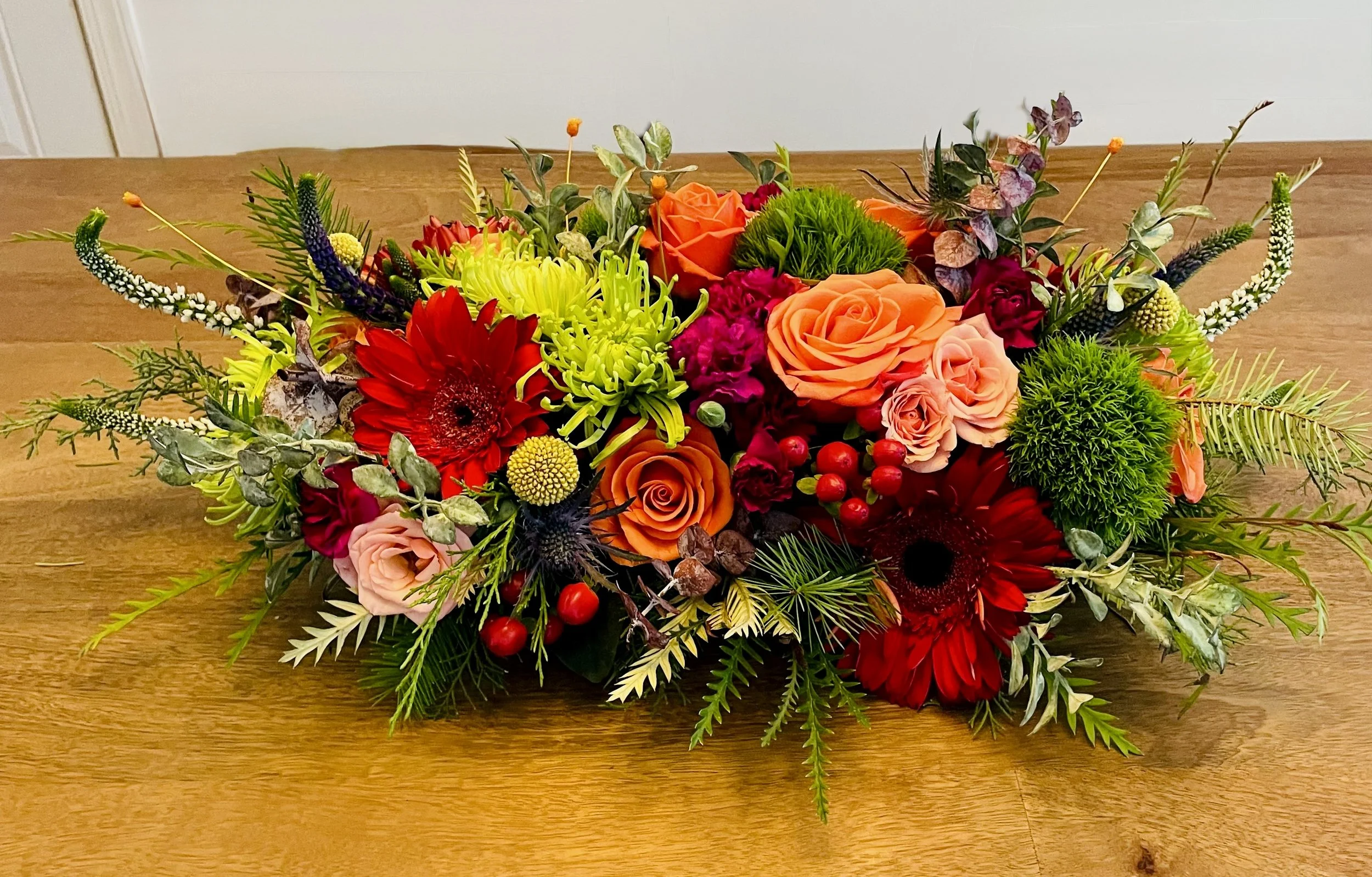 Colorful floral arrangement with red, orange, pink, purple, and green flowers on a wooden table.
