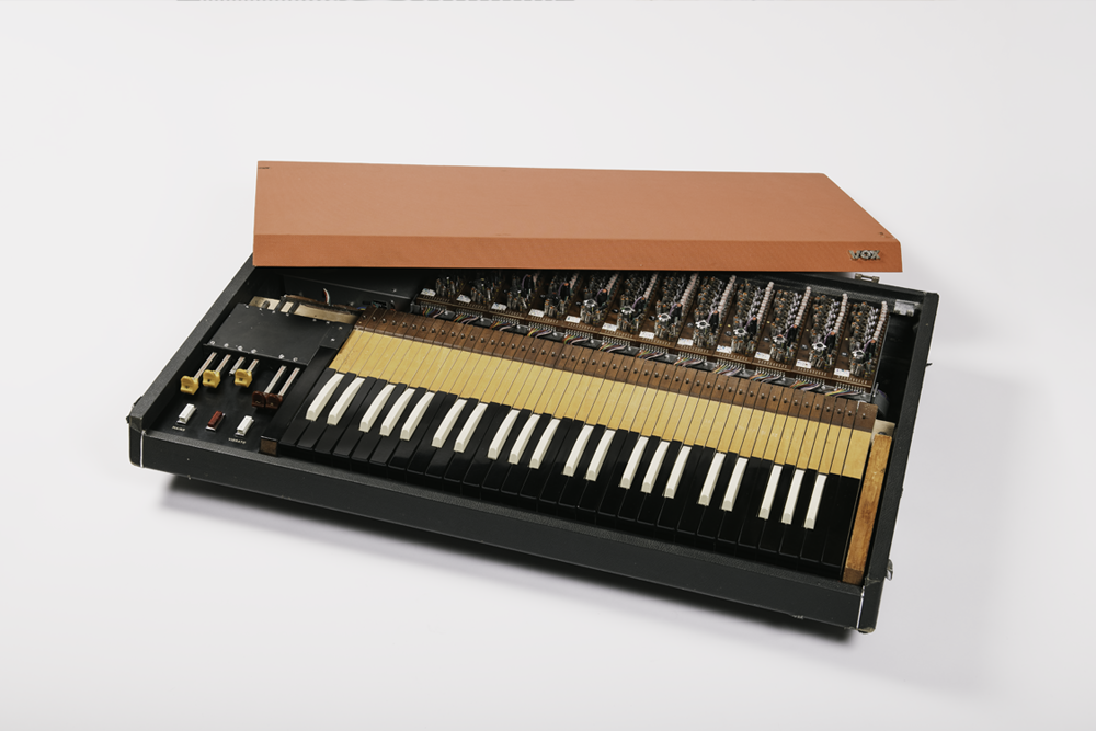 Un synthétiseur vintage avec ses touches noires et blanches, ses composants électroniques visibles et une caisse en bois, partiellement ouvert, sur un fond blanc.
