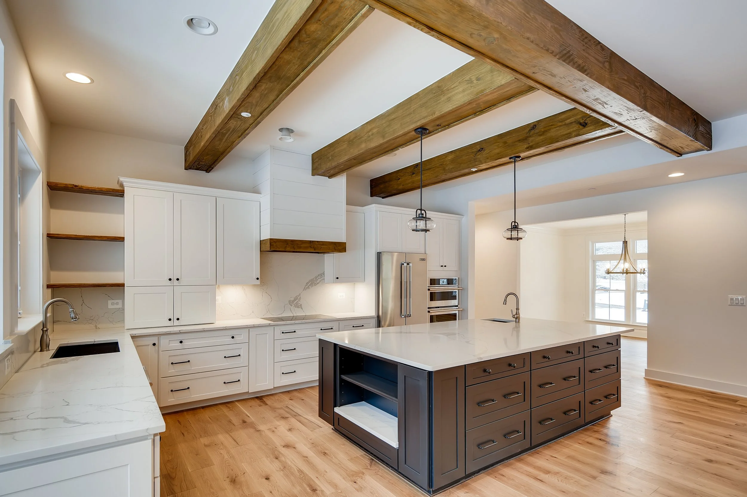 Modern kitchen with white cabinets, a black island with open shelving, a marble countertop, and exposed wooden beams on the ceiling. Hardwood floors and pendant lighting over the island.