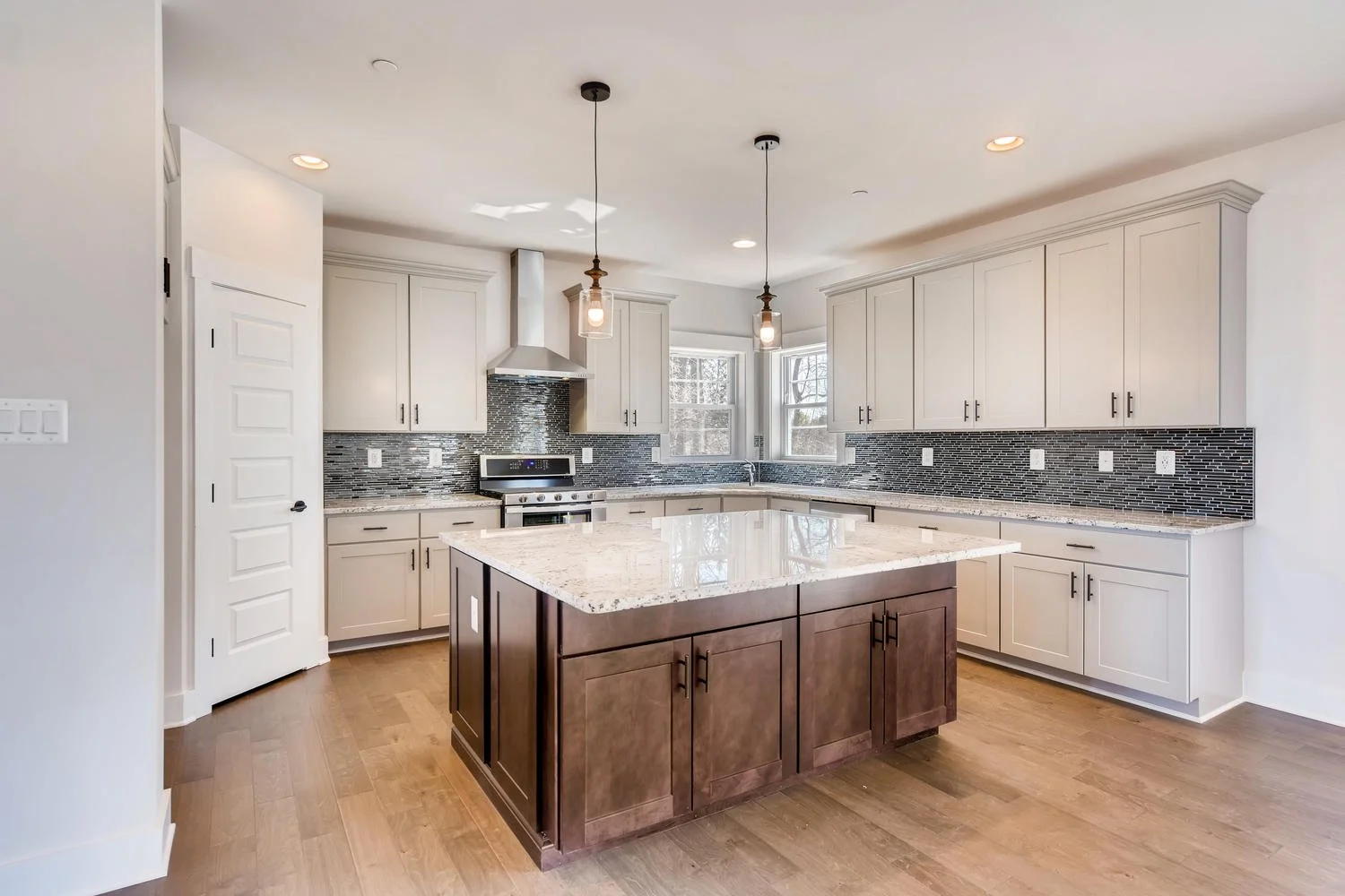 Modern kitchen with white cabinets, a dark wood island, granite countertops, stainless steel appliances, and a mosaic tile backsplash. Natural light coming through windows.