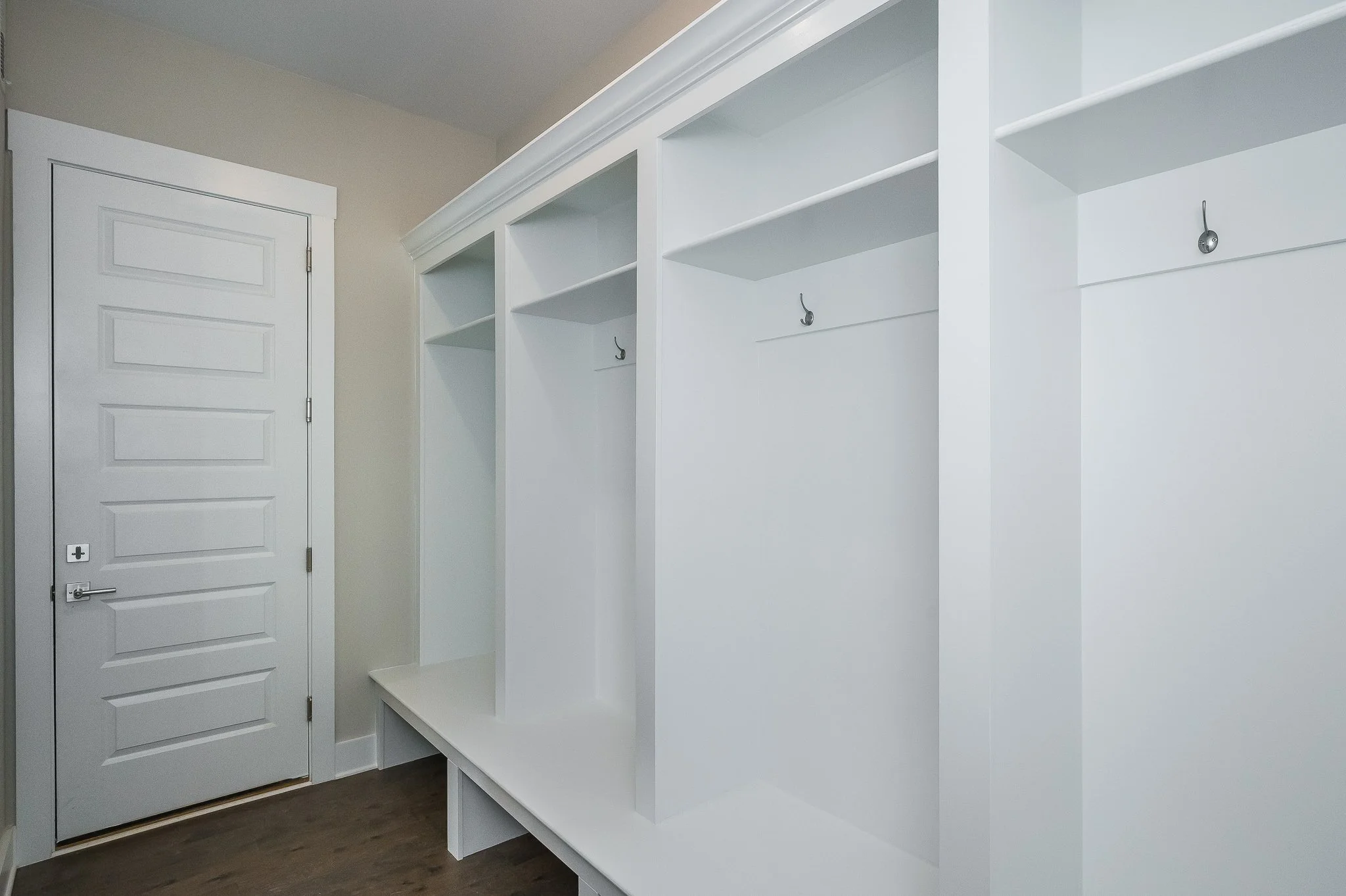 Empty built-in white closet with hooks inside and a door on the left, in a room with hardwood floors.