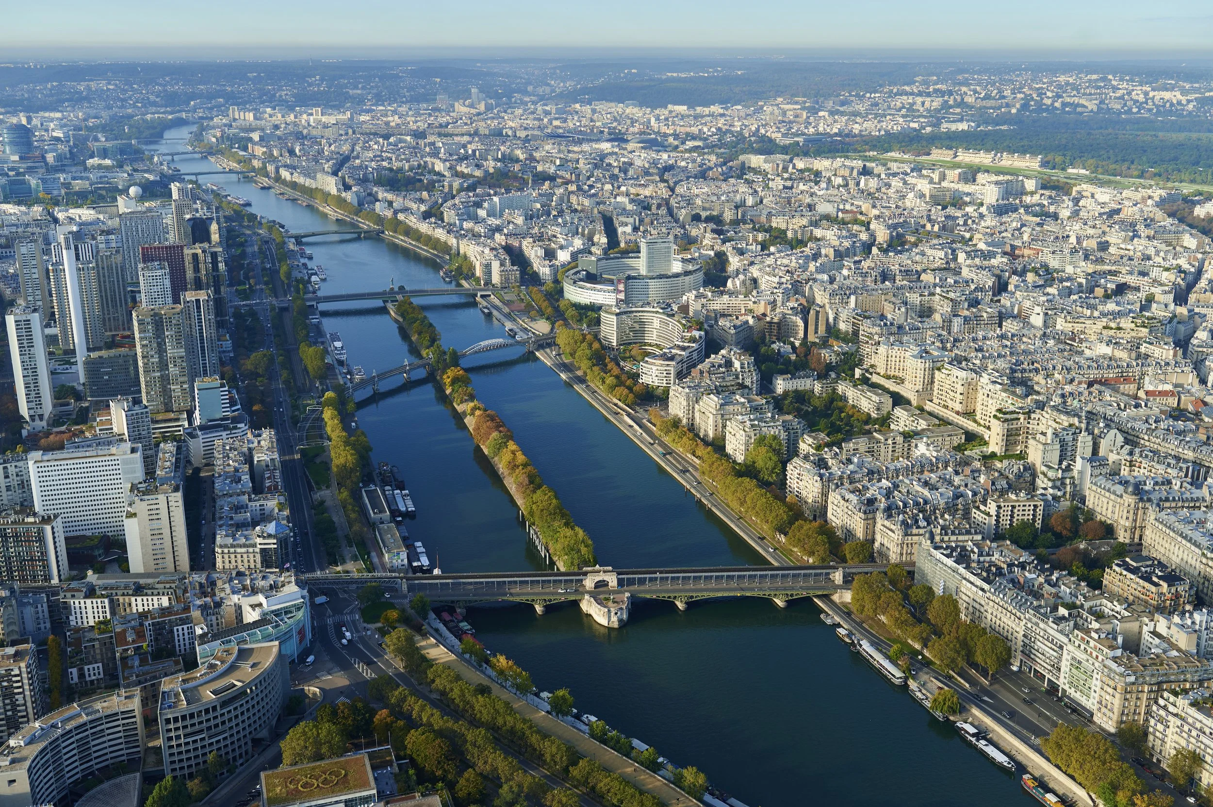 Vue aérienne de Paris avec la Seine traversant la centre-ville, entourée de nombreux bâtiments modernes et historiques, sous un ciel dégagé.