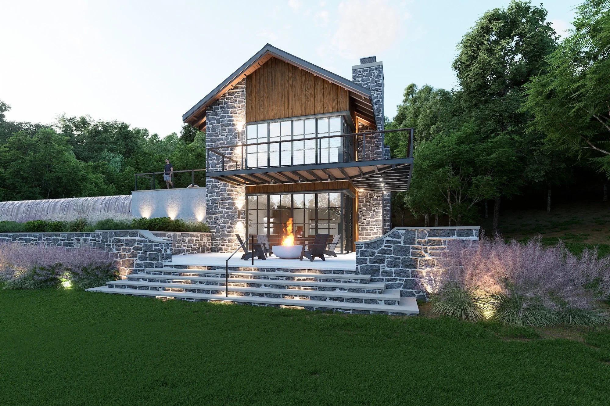 A modern two-story house with stone and wood exterior, large glass windows, and a balcony on the upper level. In front, there is a patio area with a fire pit surrounded by chairs, illuminated by outdoor lighting, with landscaped plants and a green lawn.