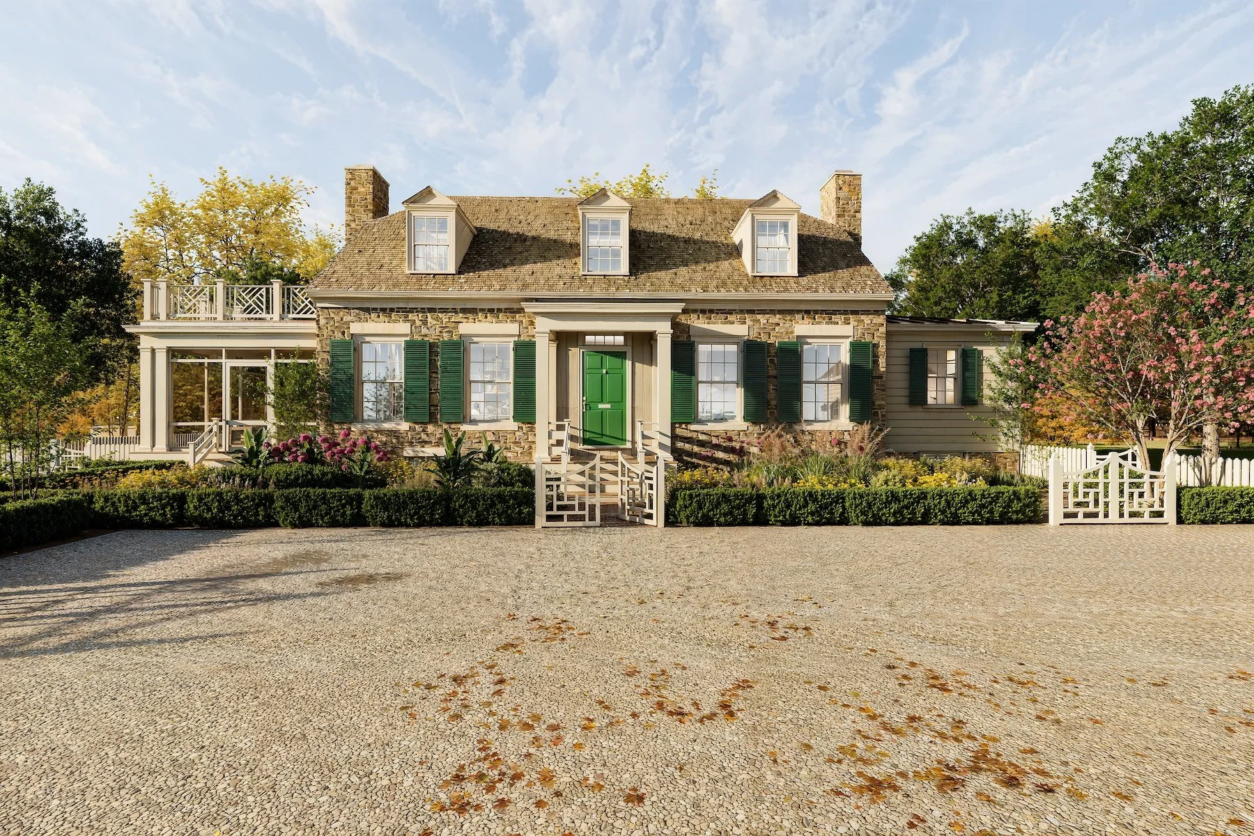 A large, historic stone house with green shutters, a green front door, and a spacious yard with colorful flowers and trees.