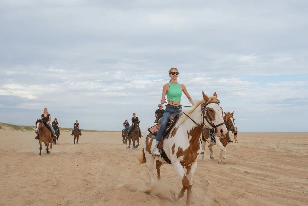 Group of people riding horses on a sandy beach under cloudy sky.