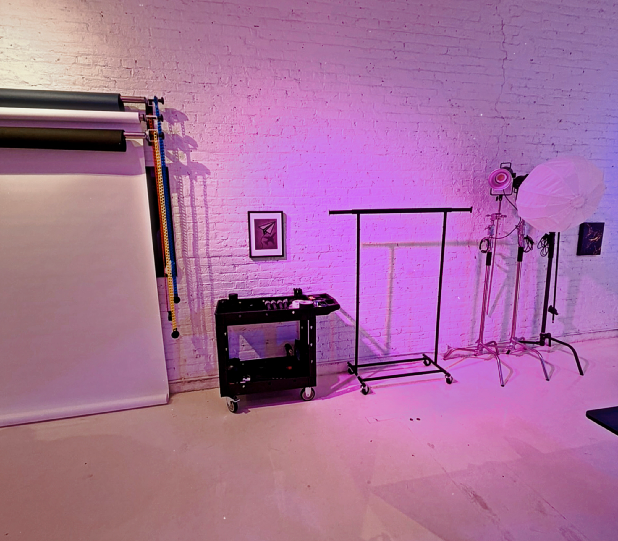 Photo studio at XYZ Studios Chicago featuring white brick wall backdrop, seamless paper backdrops, studio lighting, photo equipment cart, and clothing rack in the River North studio space.