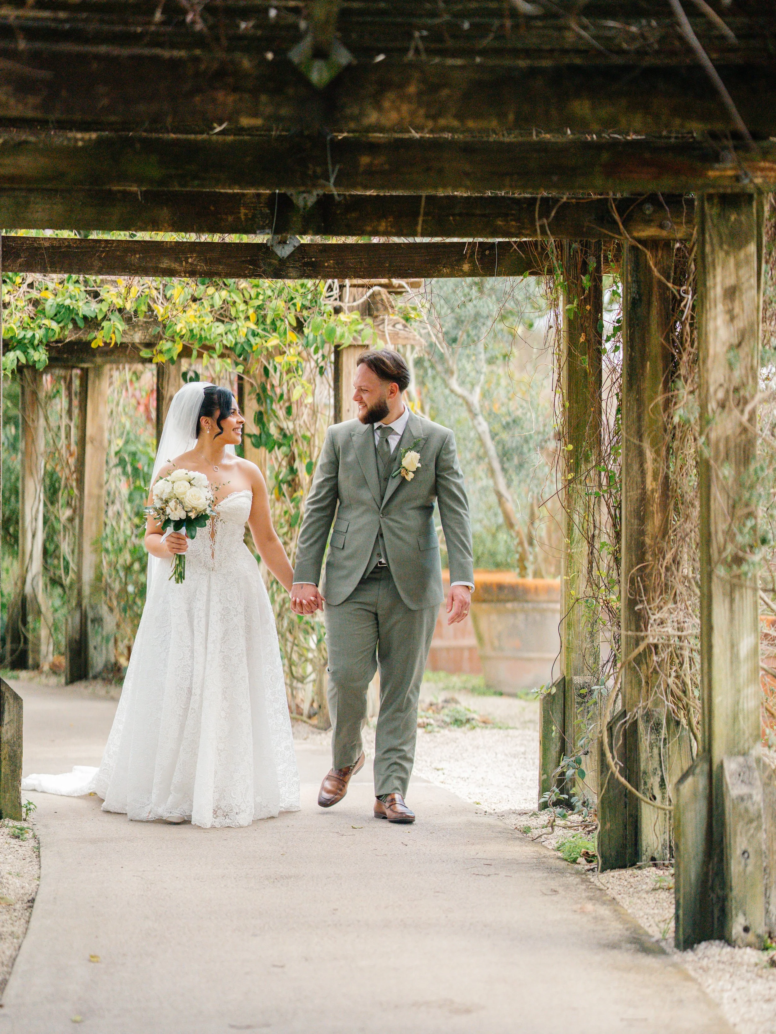 Bride and groom walking together under garden structure during South Florida wedding portraits