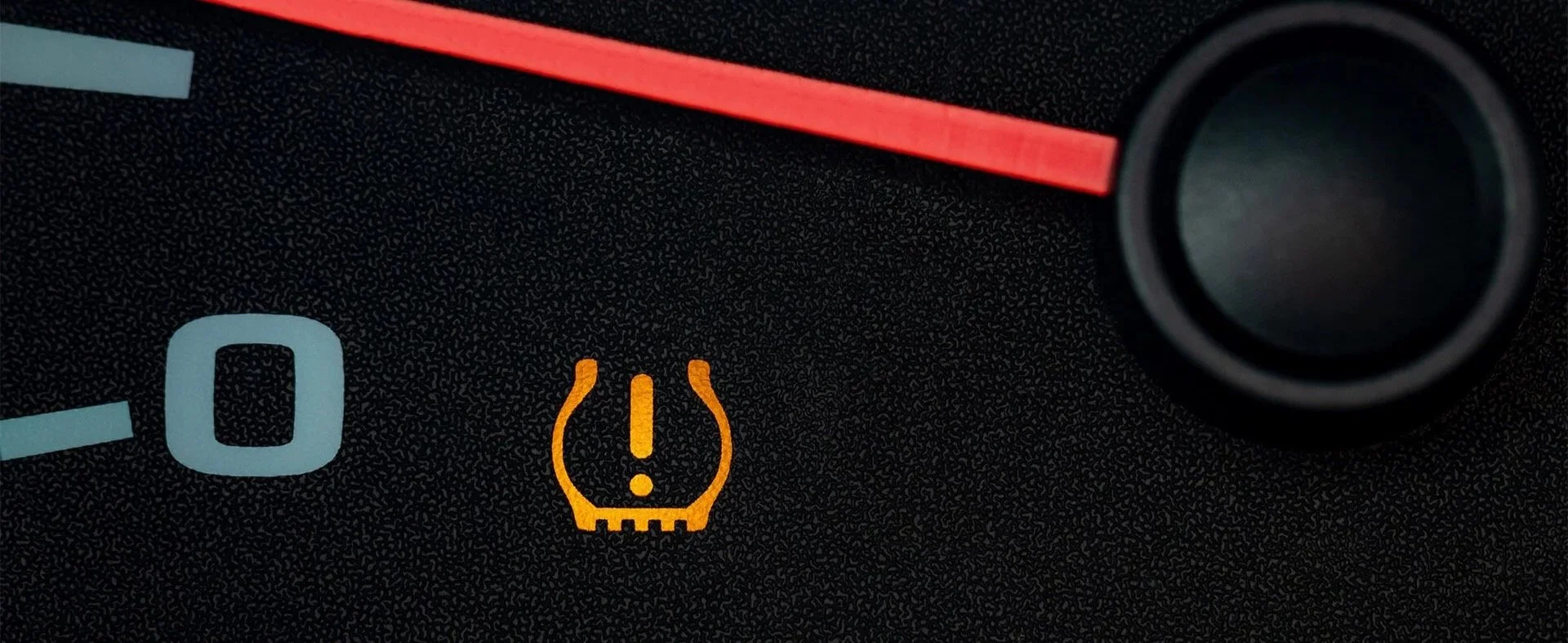 Close-up of a car dashboard with the tire pressure warning light illuminated in orange.