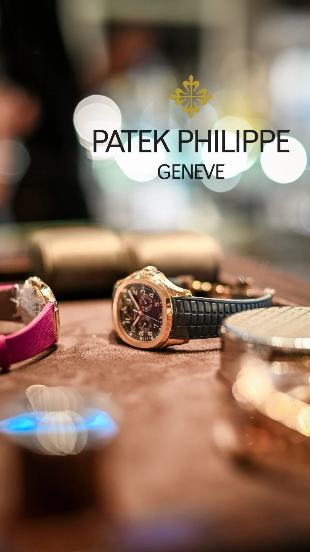 Montre de luxe avec bracelet en caoutchouc noir posée sur une surface en bois avec d'autres montres et objets flous en arrière-plan.