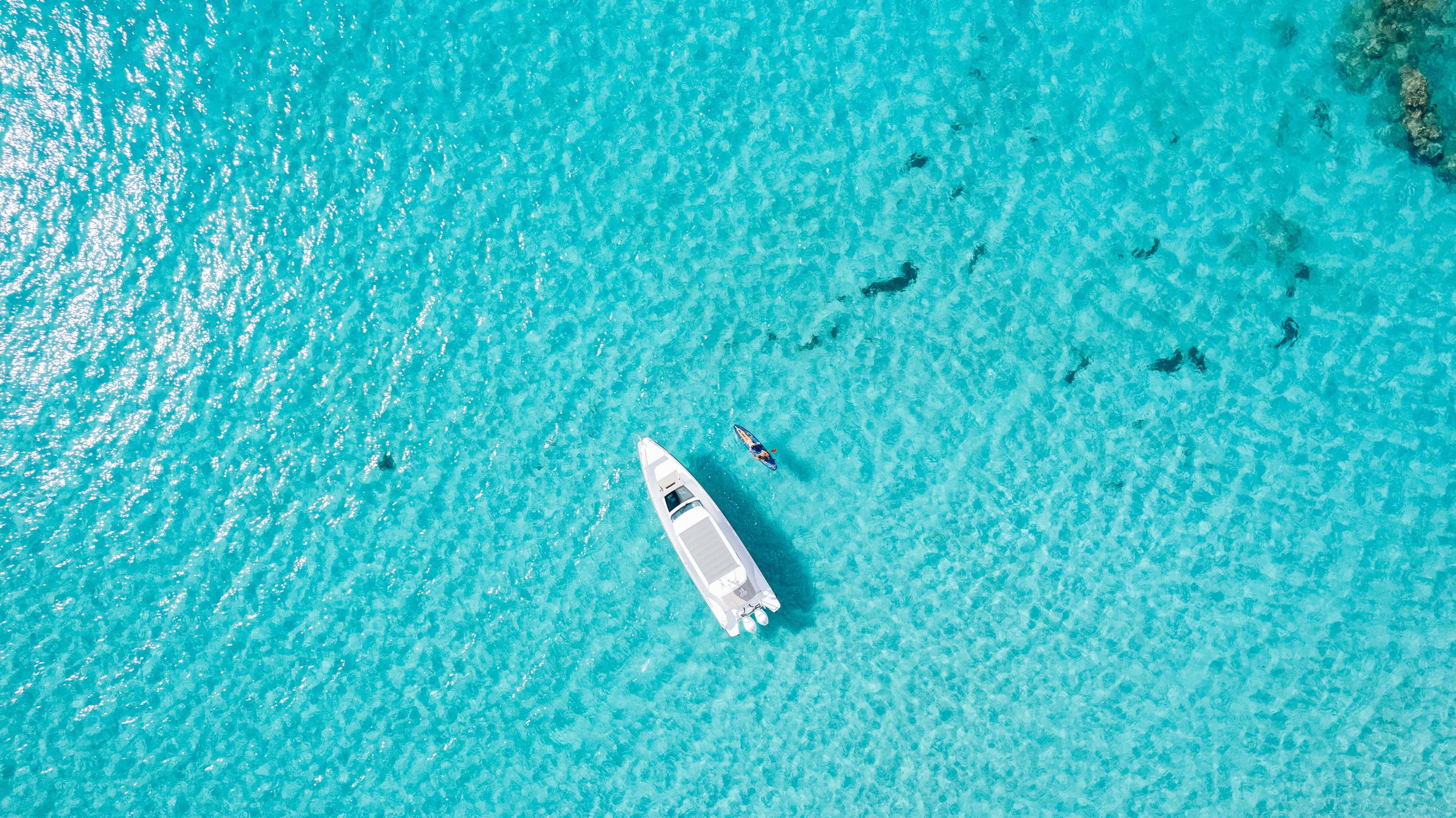 Vue aérienne d'une mer turquoise avec un yacht blanc et deux kayaks, vue depuis le ciel.