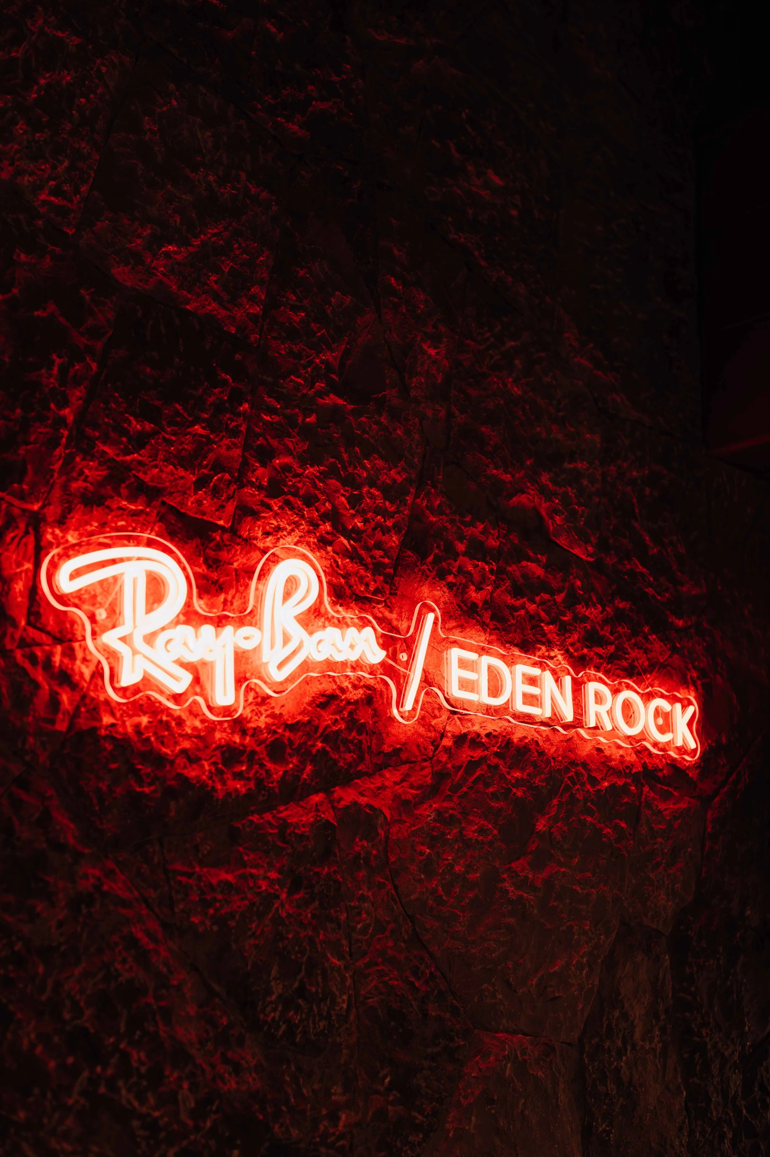 Neon rouge affichant le texte "Rayon Bain / Eden Rock" sur un mur en pierre sombre.