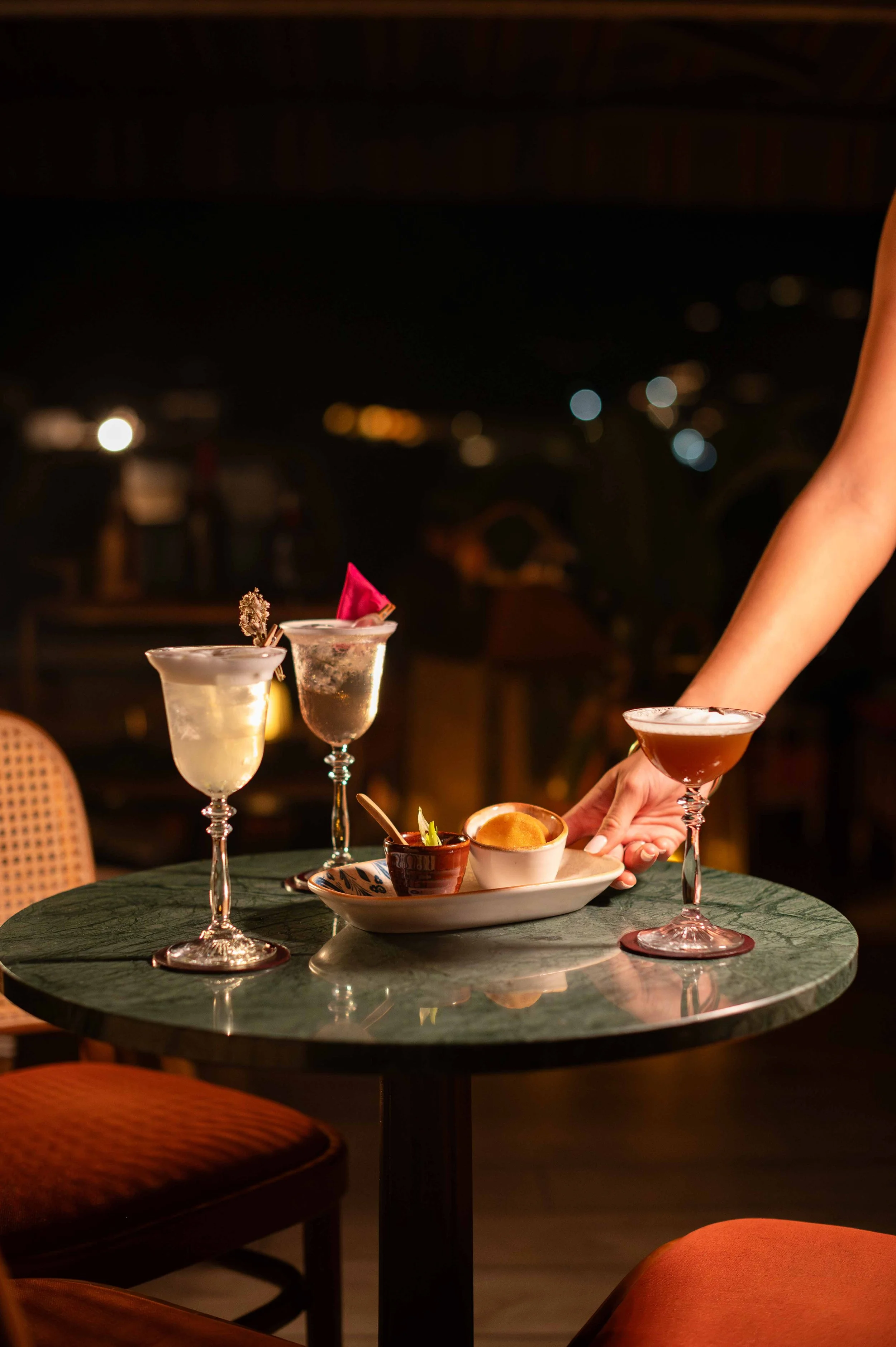 Verre à cocktail, assiette avec des sauces, mains d'une personne en train de servir un cocktail dans un restaurant ou bar en soirée.